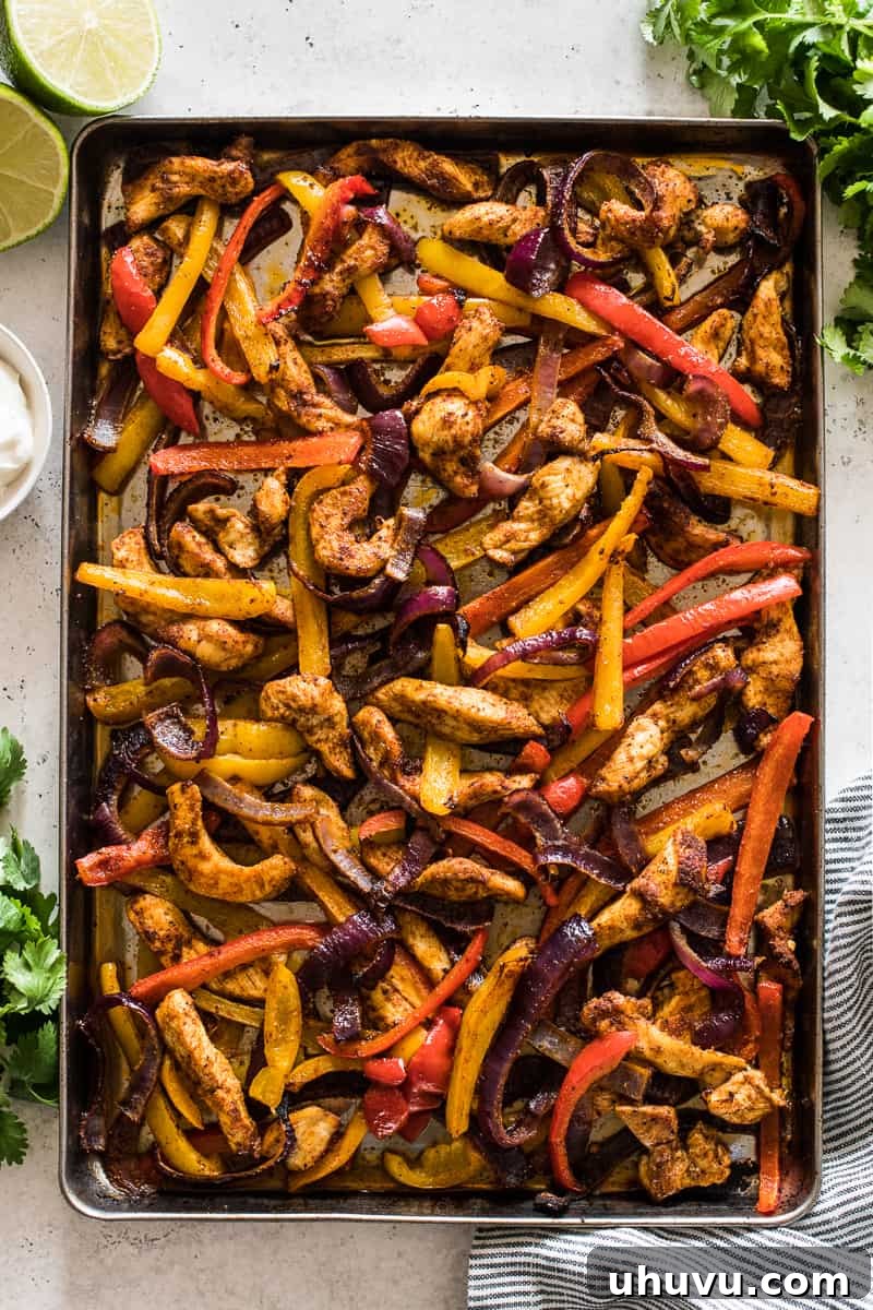 Sheet pan chicken fajitas on a table with cilantro, sour cream, and lime juice.