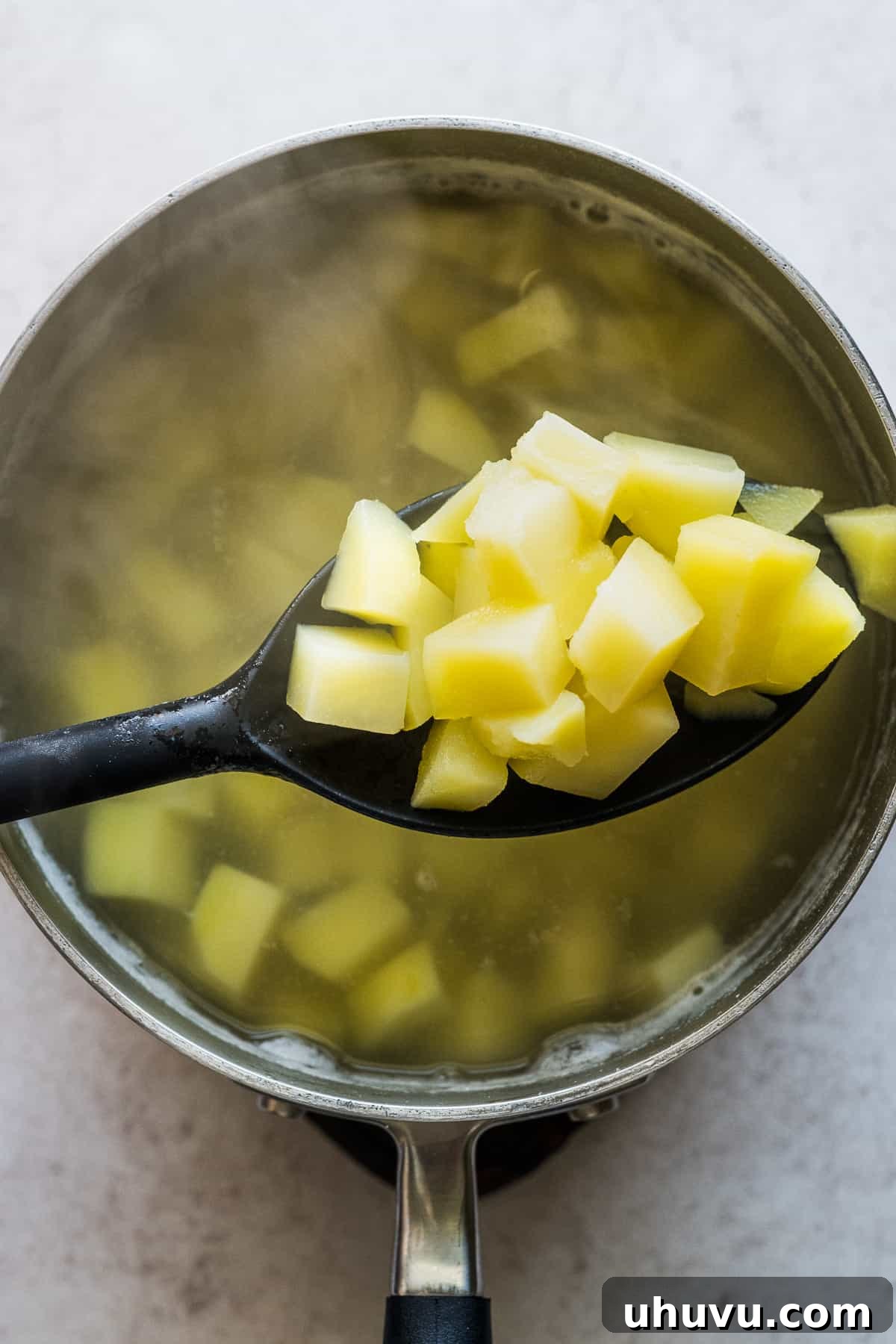 Cooked and tender potato cubes on a spoon, ready for the filling.