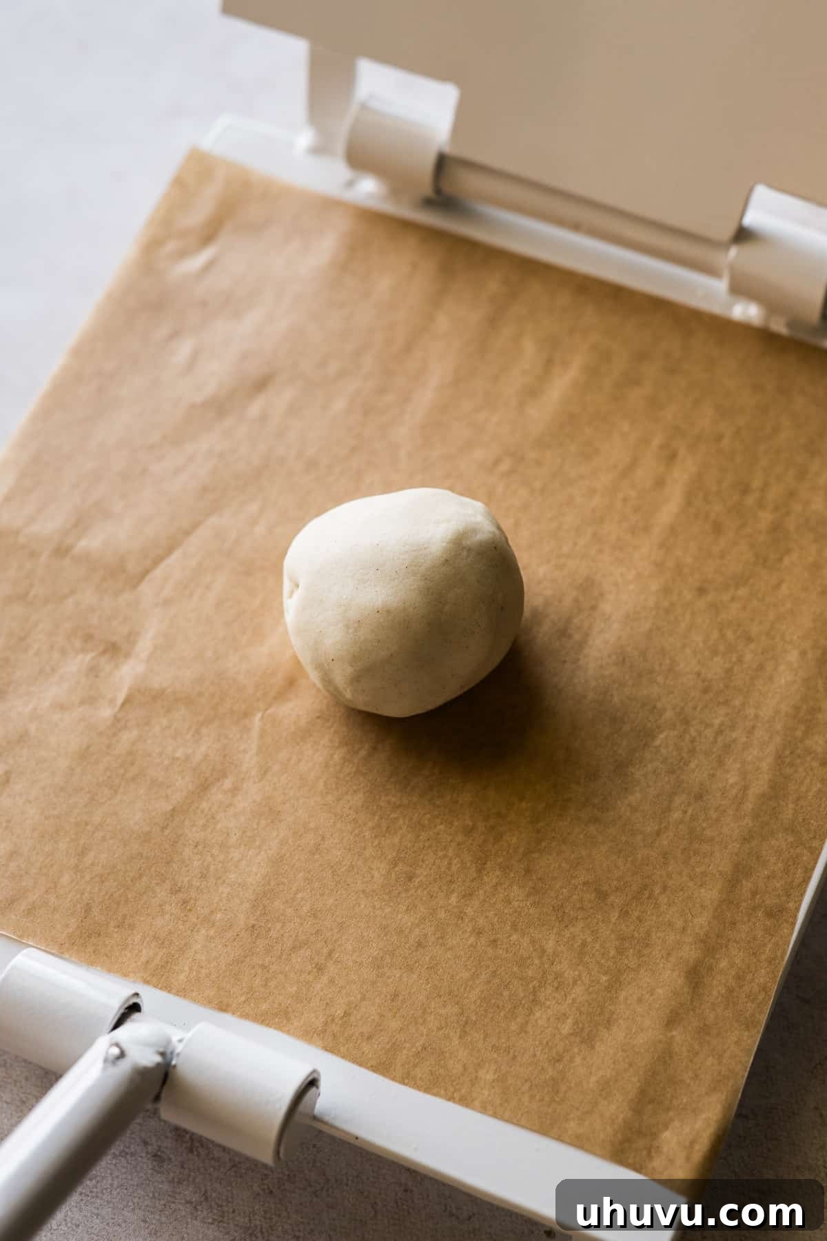 A ball of masa dough placed on a tortilla press lined with parchment paper.