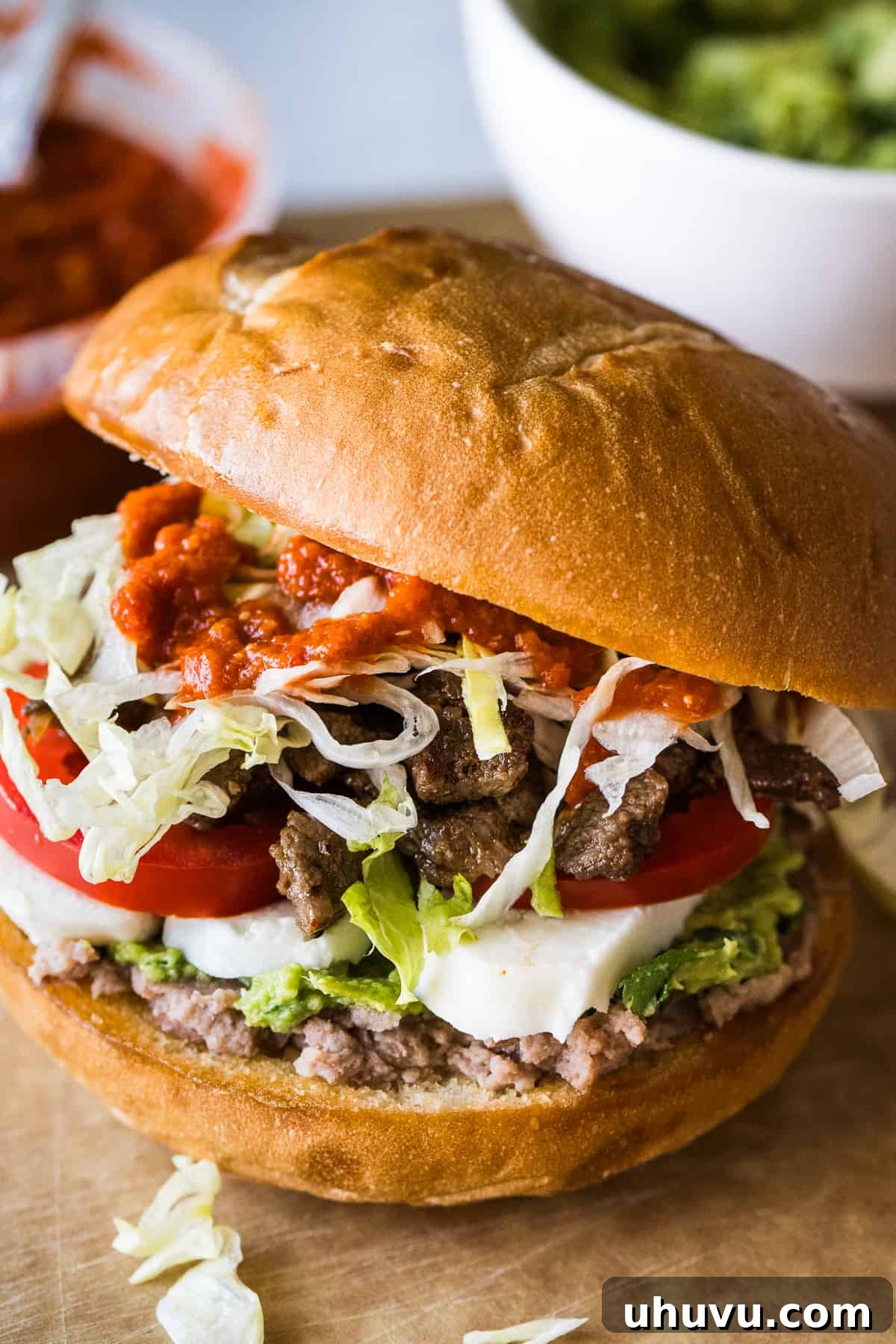 Authentic Mexican Torta 15 A perfectly assembled Torta, showcasing layers of refried beans, guacamole, queso fresco, tomato, steak, lettuce, and salsa.