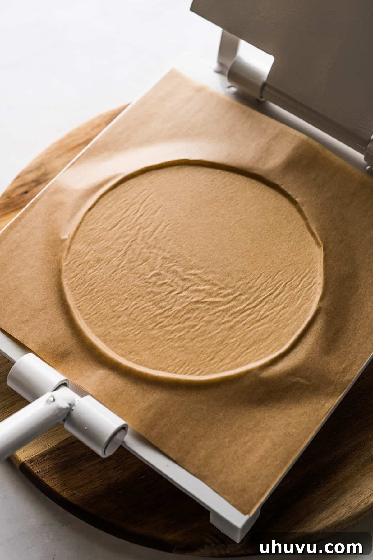 Golden Fried Cheesy Pockets 7 A perfectly flattened ball of masa dough, covered with parchment paper, positioned on a tortilla press.