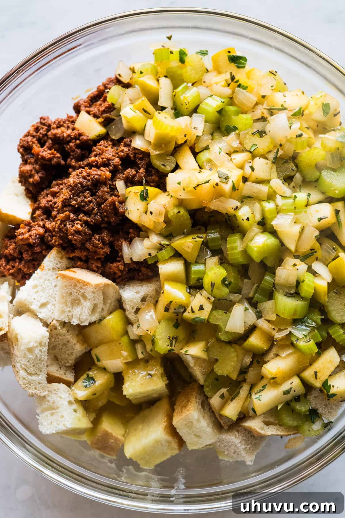 Spicy Chorizo Stuffing 7 A large mixing bowl containing cubed sourdough bread, cooked chorizo, sautéed vegetables and apples, melted butter, broth, and beaten eggs, before being mixed.