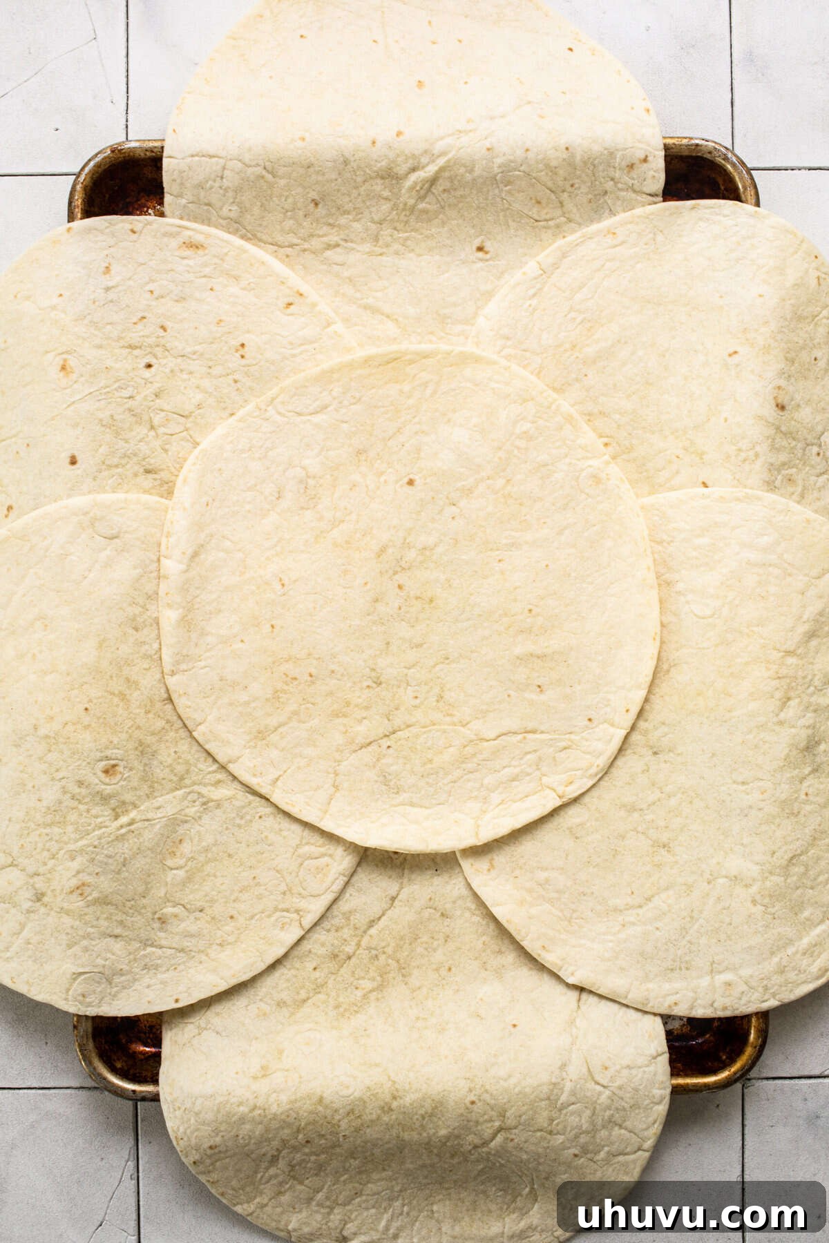 Large flour tortillas carefully arranged on a sheet pan, with six tortillas overlapping the edges and one placed in the center, forming the base for a giant quesadilla.