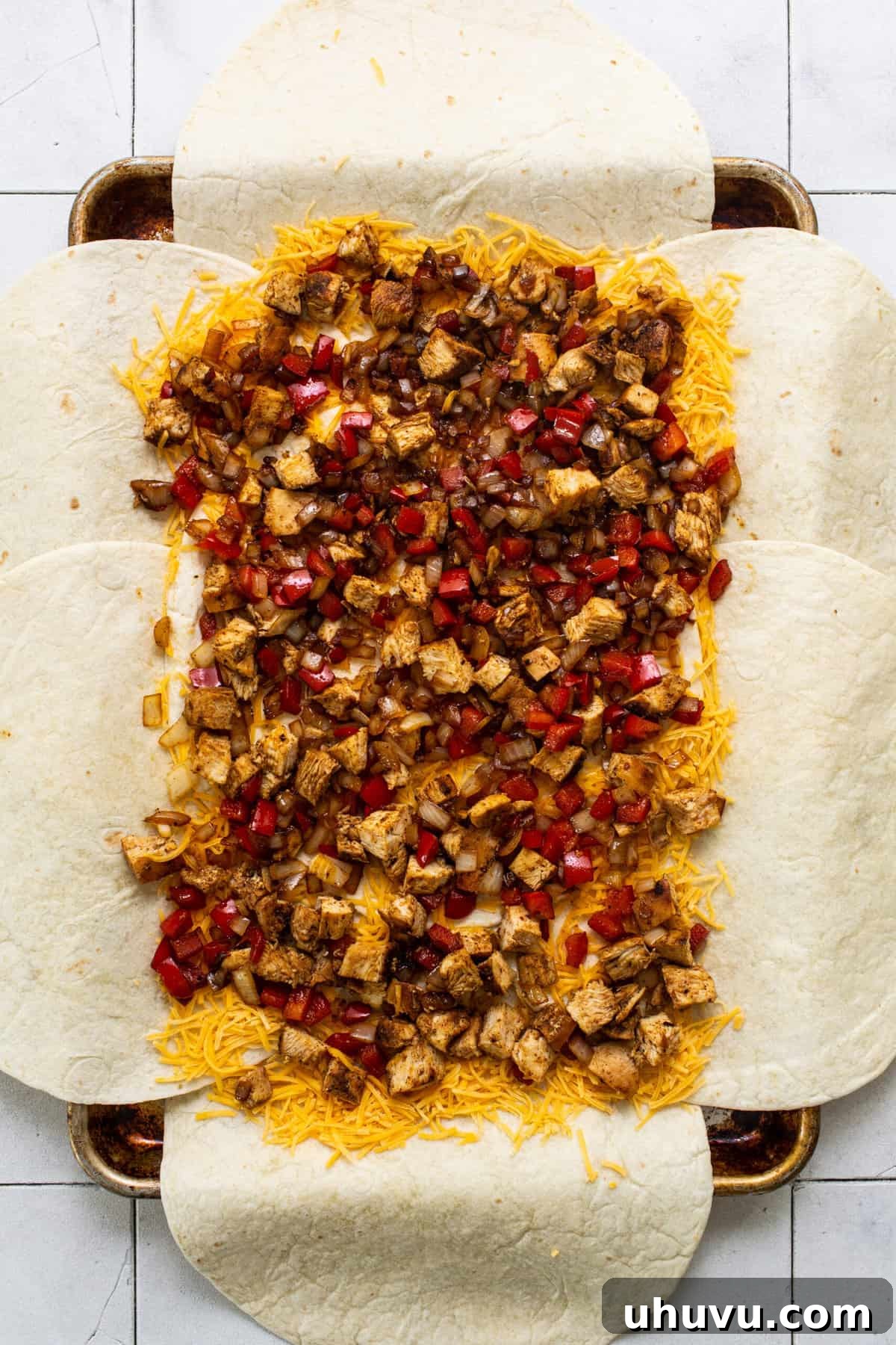 Close-up of the sheet pan quesadilla filling, showing cooked and diced chicken, vibrant bell peppers, onions, and a generous layer of shredded cheese atop the flour tortillas before folding.