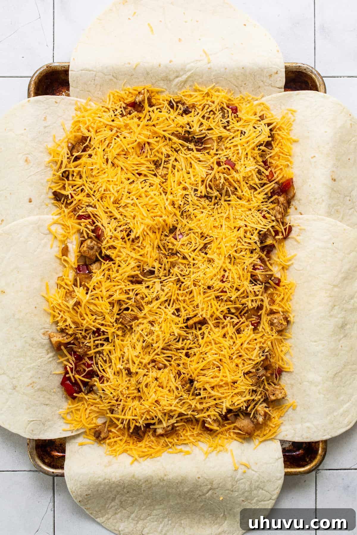 The sheet pan quesadilla prepared with layers of cheese, chicken, and vegetables, ready for the outer tortillas to be folded inward for baking.
