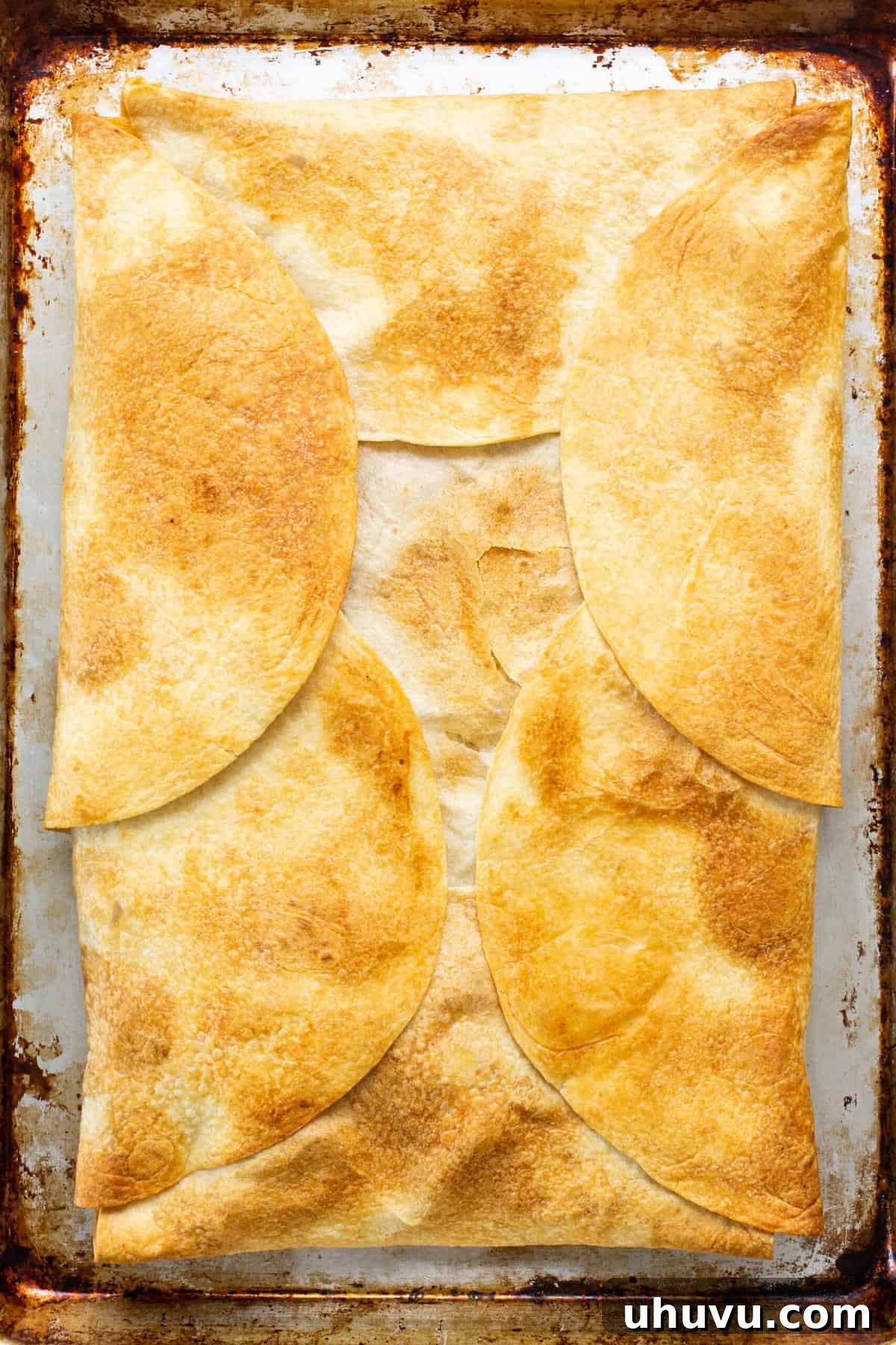 A large, golden-brown and perfectly crispy sheet pan quesadilla, freshly baked and ready to be sliced, sitting on a baking sheet.