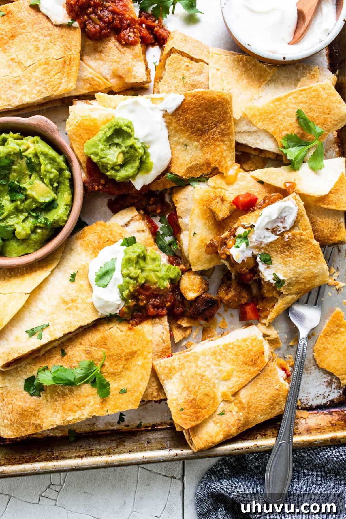 Freshly baked sheet pan quesadillas, expertly sliced into individual triangular servings, adorned with generous dollops of sour cream and scoops of rich guacamole.