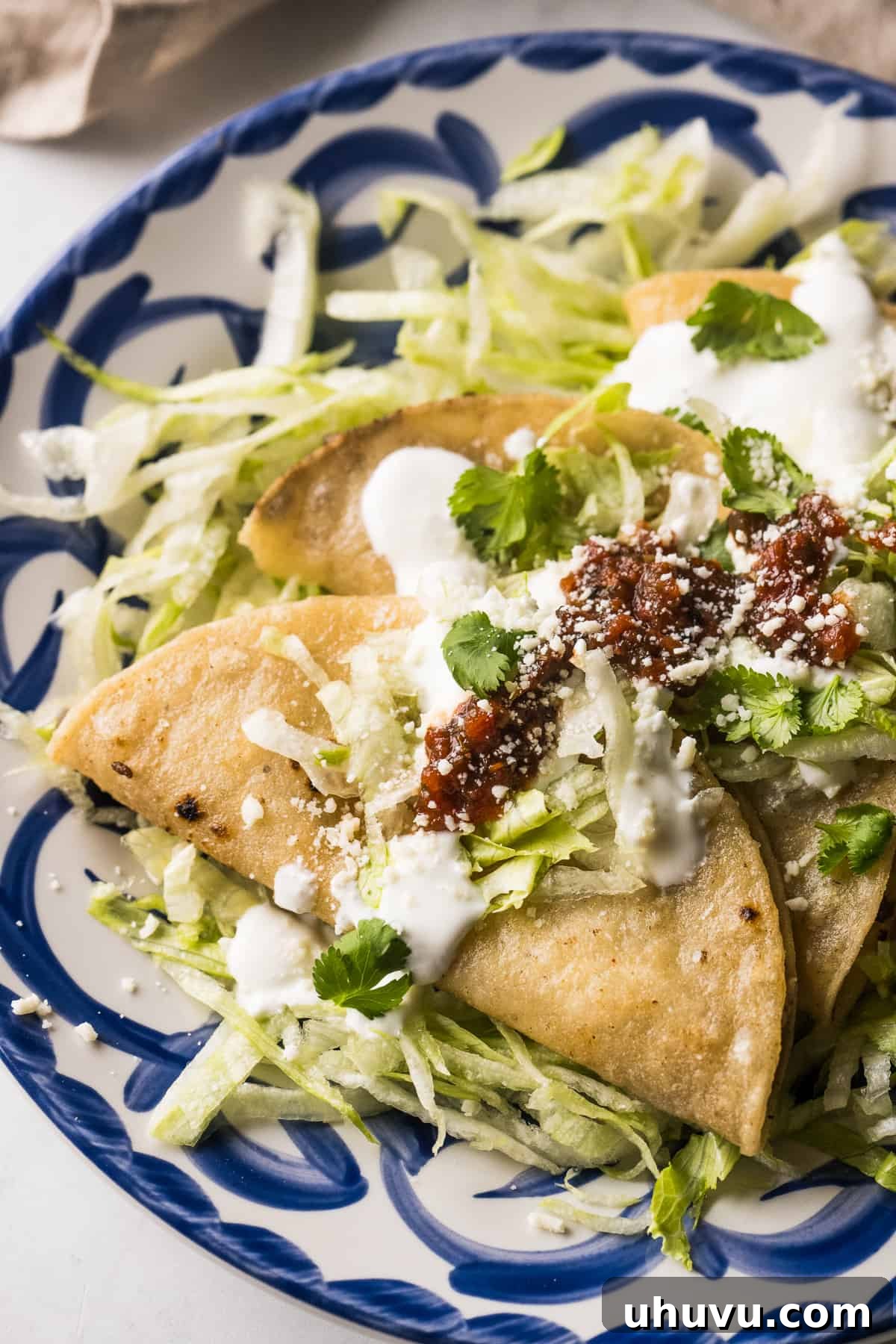 Golden Crispy Tacos 10 Tacos dorados on a plate served with mexican crema, red salsa, and shredded lettuce.