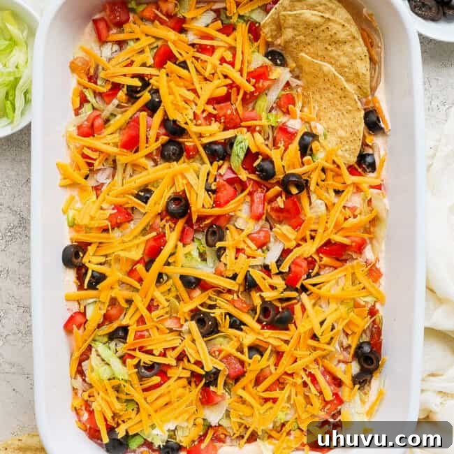 Taco dip in a baking dish topped with shredded cheese, tomatoes, and olive served with tortilla chips.