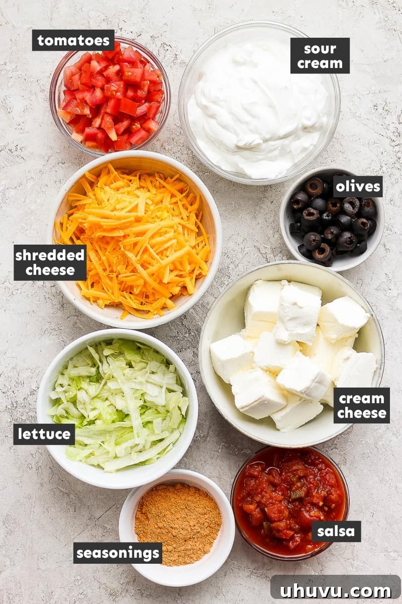 Ultimate Taco Party Dip 3 Fresh ingredients for taco dip, including cream cheese, sour cream, taco seasoning, salsa, and various chopped vegetables, laid out on a table, ready for assembly.