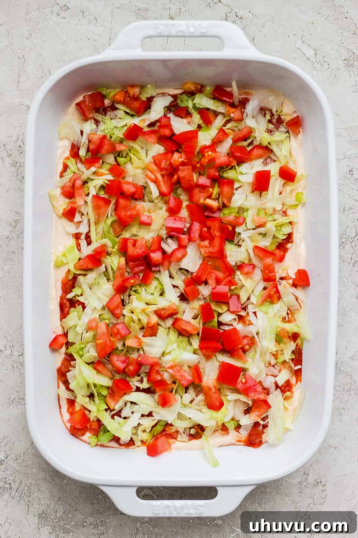 Ultimate Taco Party Dip 8 Freshly shredded lettuce and diced tomatoes layered beautifully in a baking dish, adding vibrant color and texture to the taco dip.