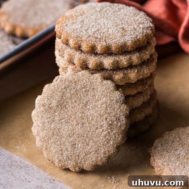 Biscochitos covered in cinnamon sugar stacked on top of one another on a piece of parchment paper.