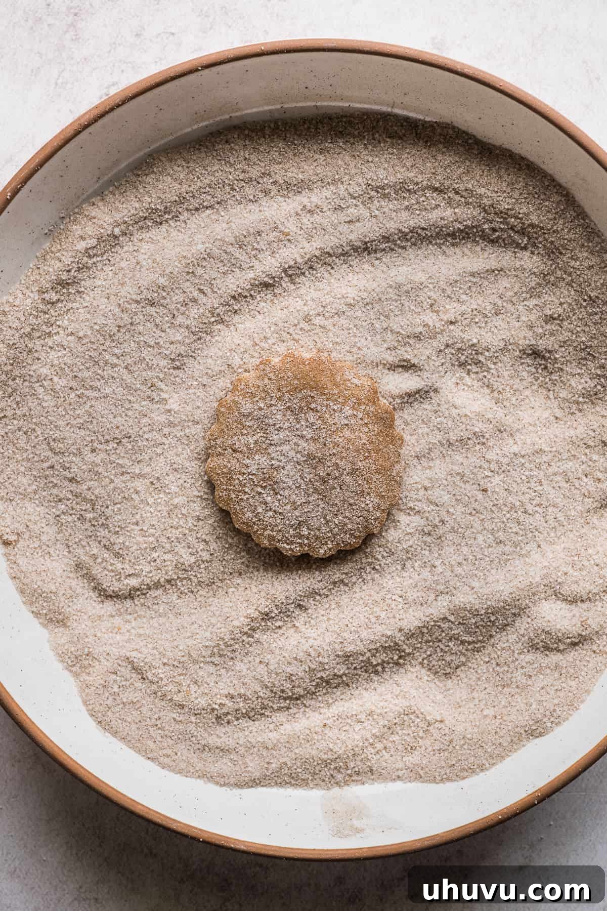 A biscochito being covered in cinnamon sugar topping.