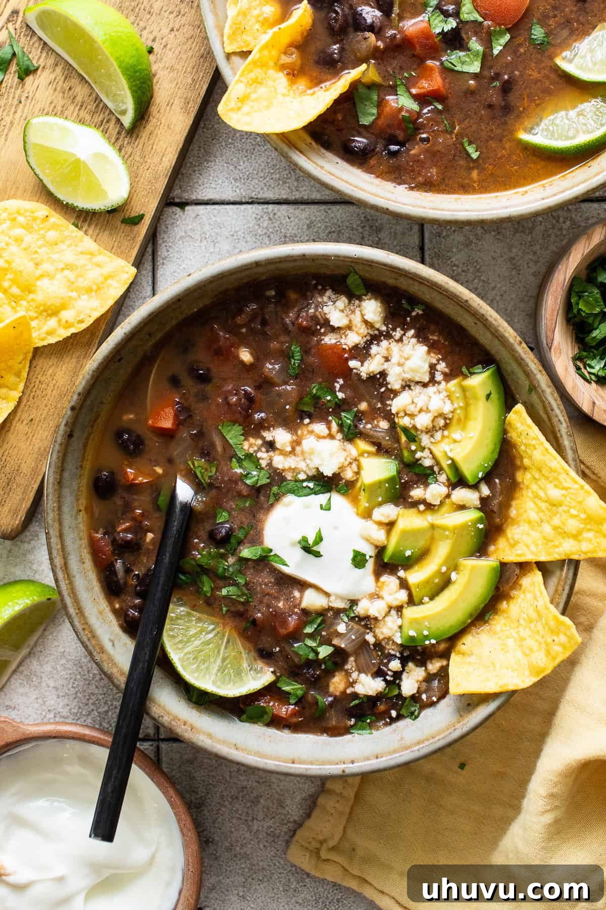 A bowl of black bean soup topped with sour cream, avocados, and cilantro.