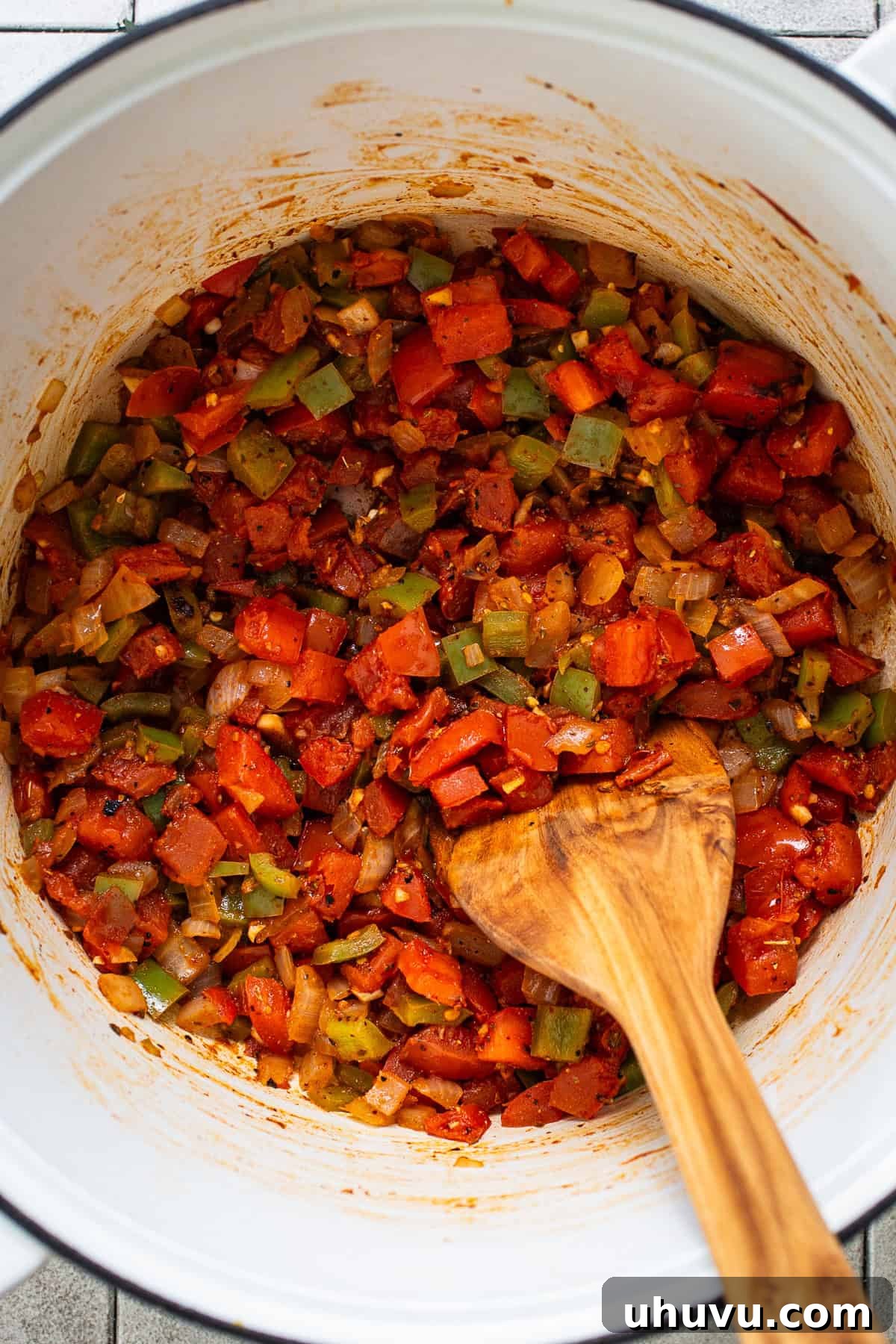 Tomatoes, peppers, and onions cooking in a pot.