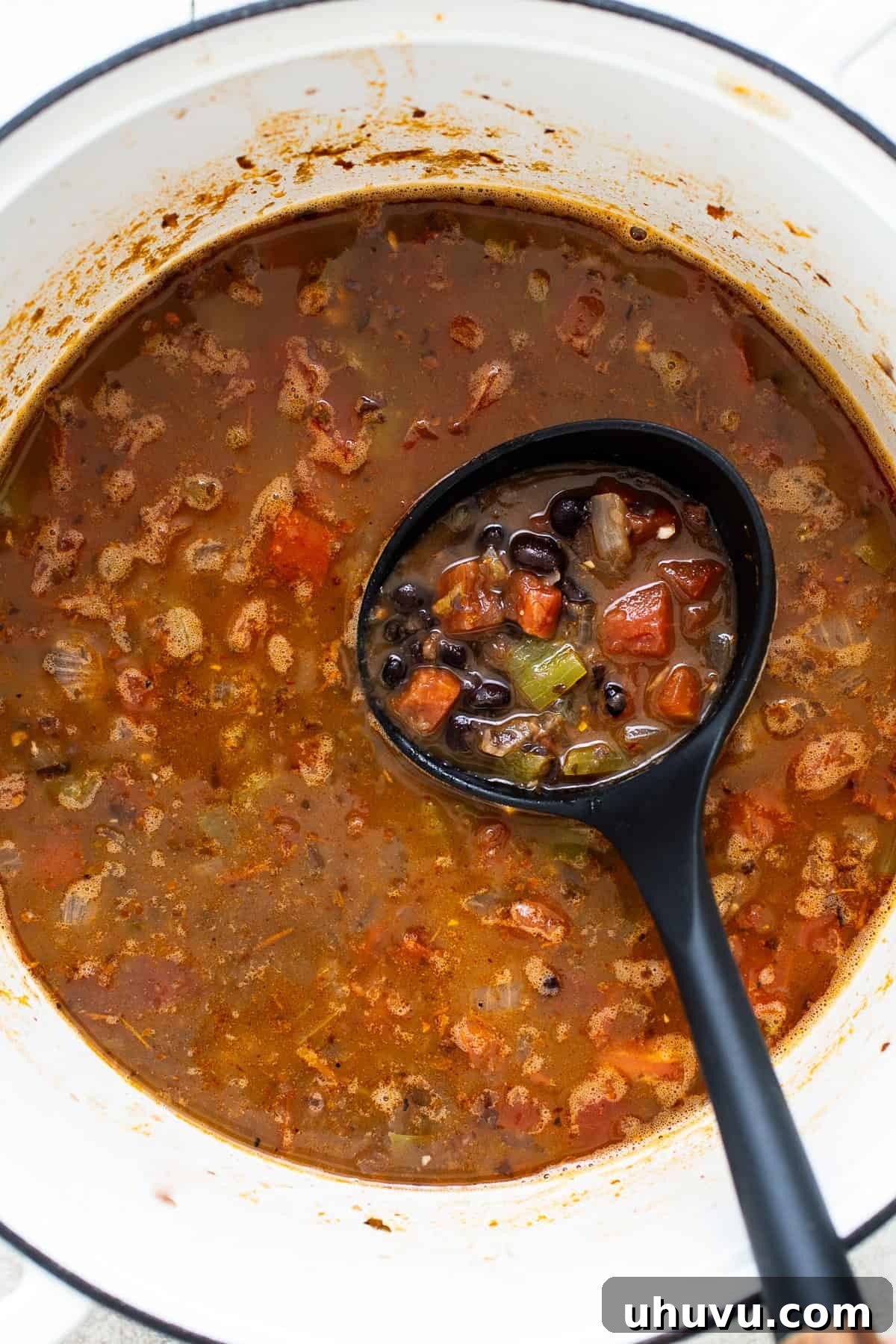 A ladle with black bean soup in a pot ready to be served.