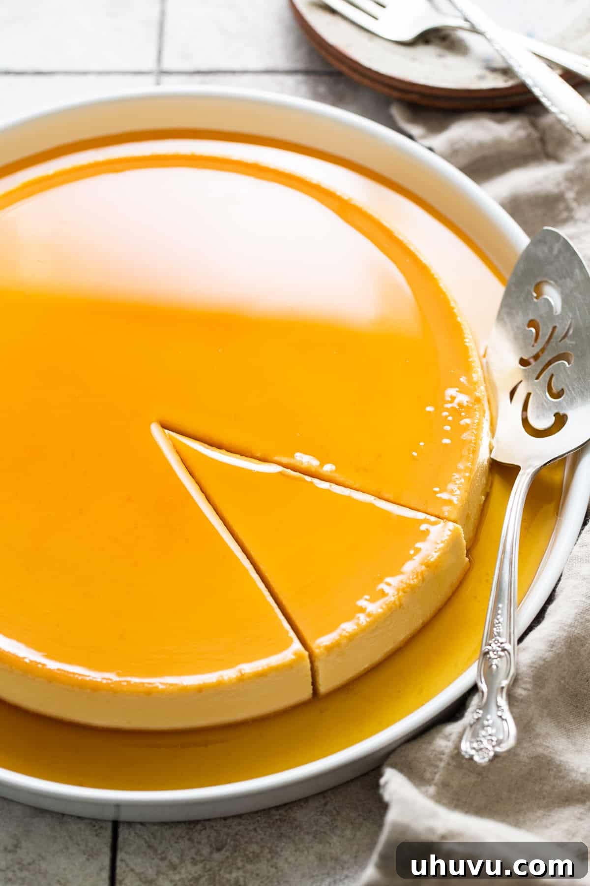 Rich Cheese Flan 2 A slice of creamy Flan de Queso with a glistening caramel sauce on top, presented on a white serving plate, with a portion already removed, showcasing its smooth texture.