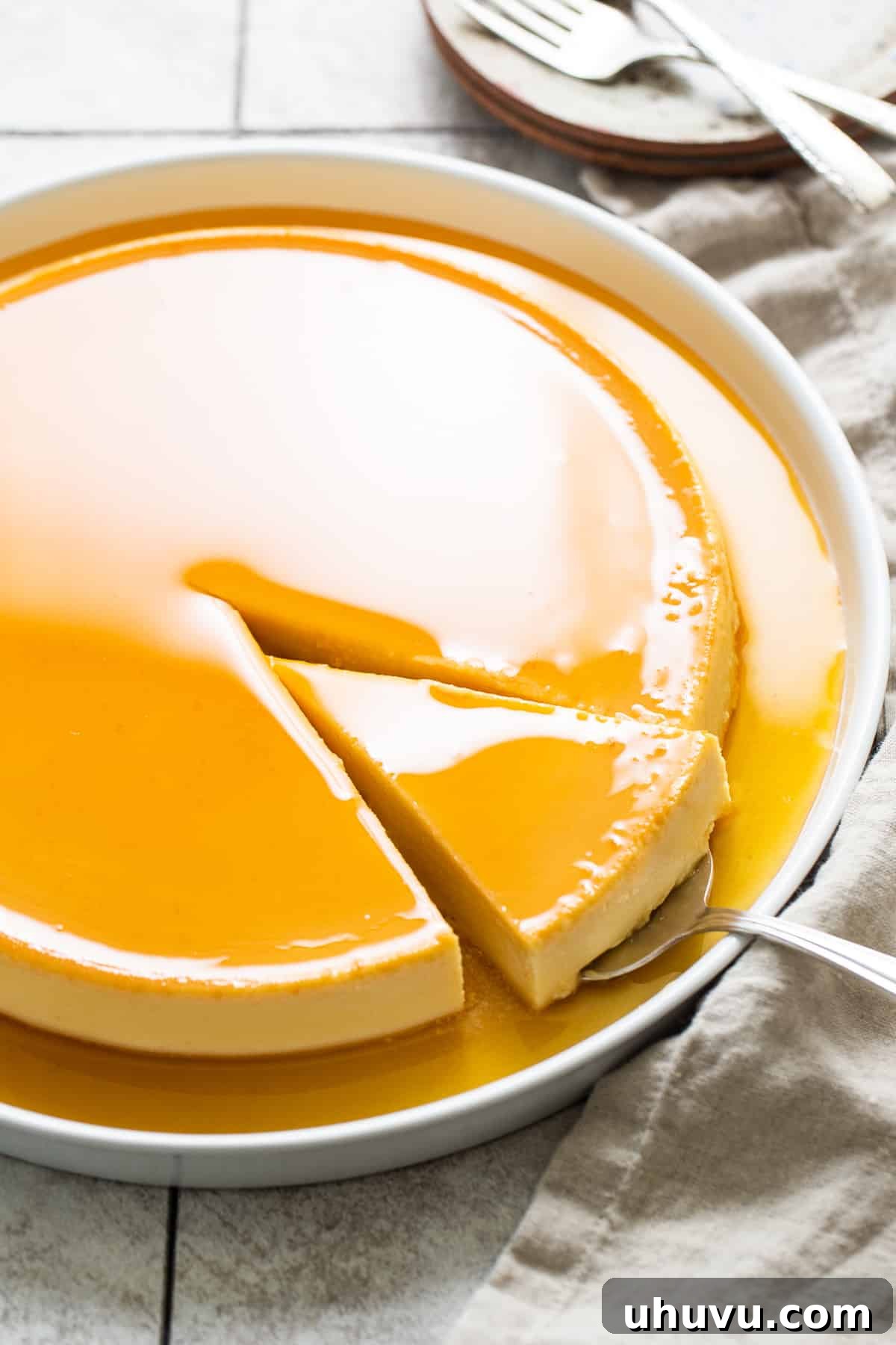 Rich Cheese Flan 7 A serving spoon gracefully holding a single, perfect slice of Flan de Queso, showcasing its smooth texture and rich caramel topping, ready to be enjoyed.