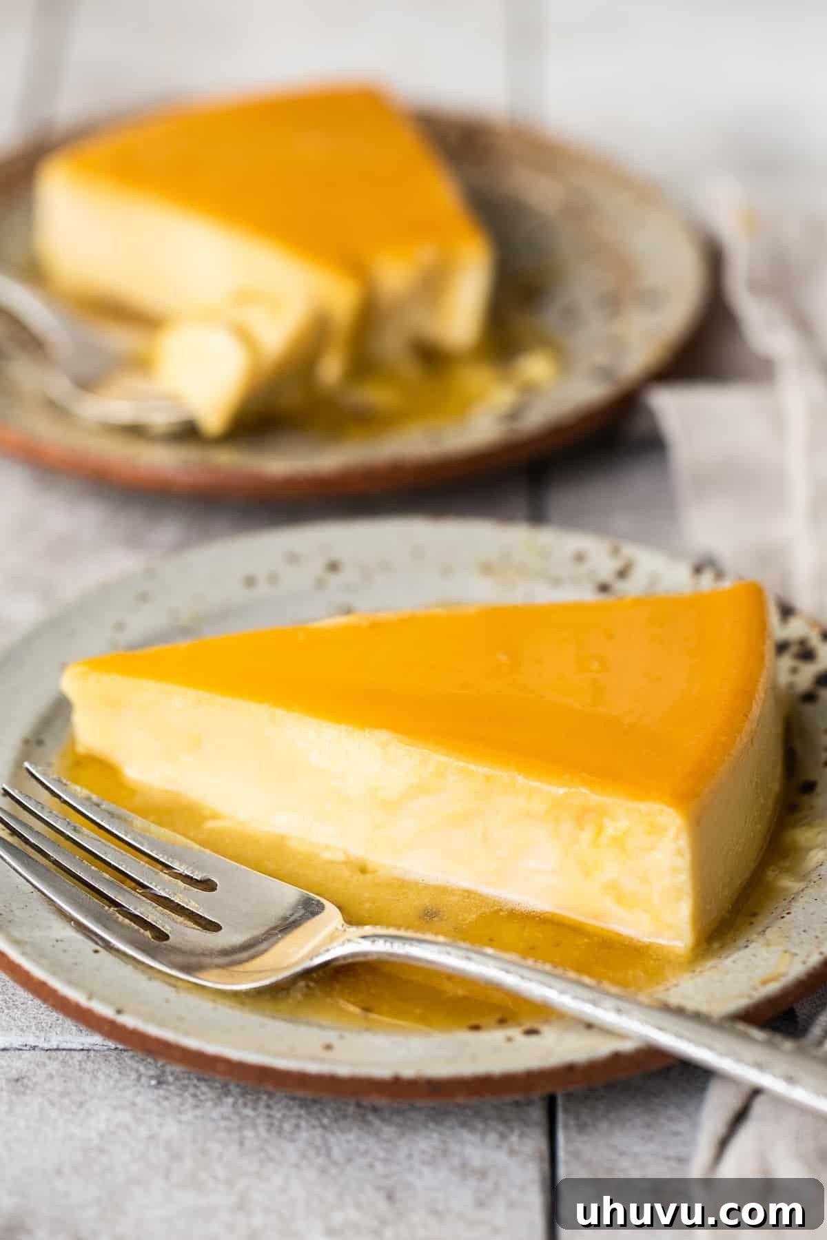 Rich Cheese Flan 8 A pristine slice of creamy, smooth Flan de Queso, generously coated with a rich, amber caramel sauce, resting on a white plate beside a fork, inviting a delicious bite.