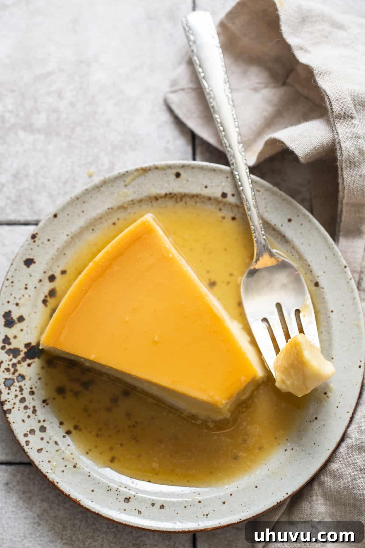 Rich Cheese Flan 9 A delicious piece of smooth Flan de Queso gracefully balanced on a fork, ready to be enjoyed, with the dessert resting on a white plate in the background.