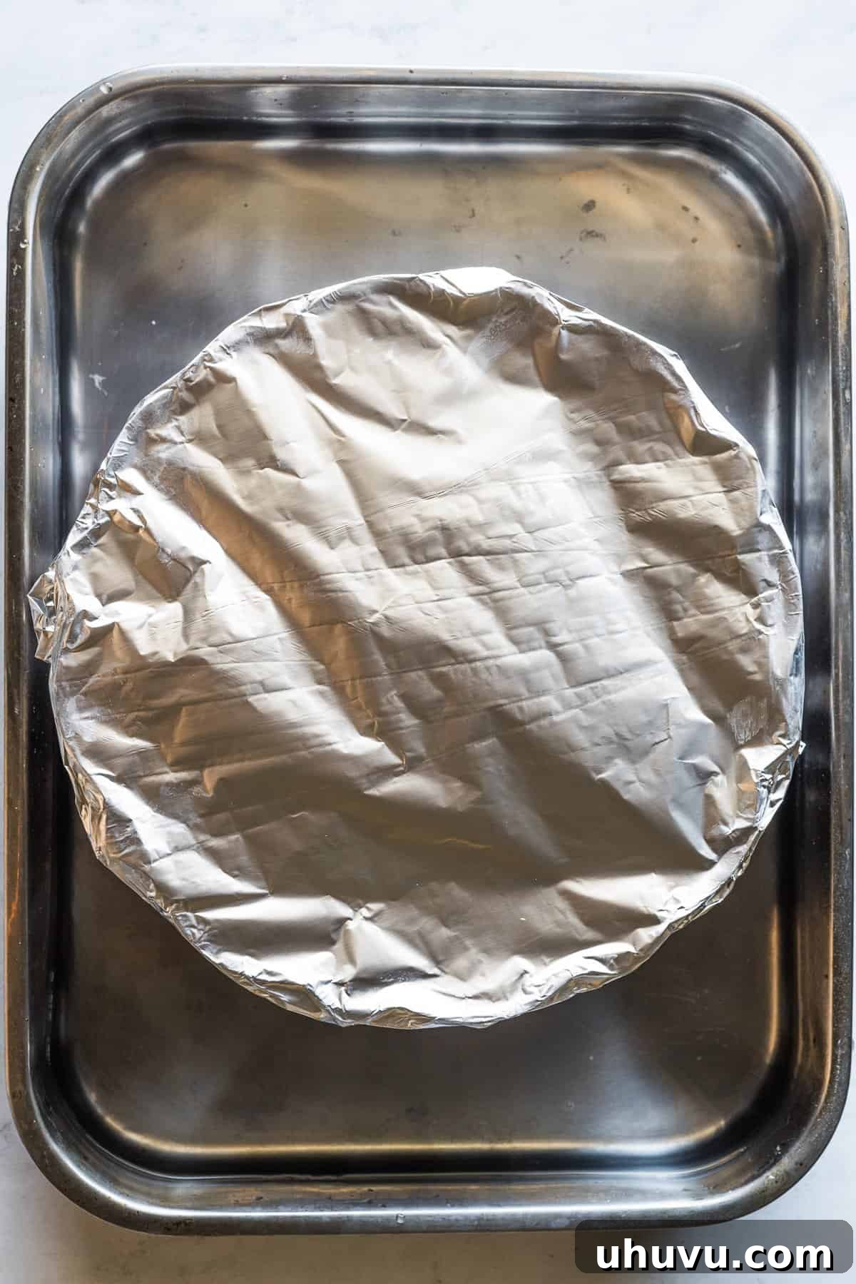 Chocolate Flan Fusion 11 A bundt pan, securely covered with foil, rests within a larger roasting pan filled with a water bath, ready for baking.