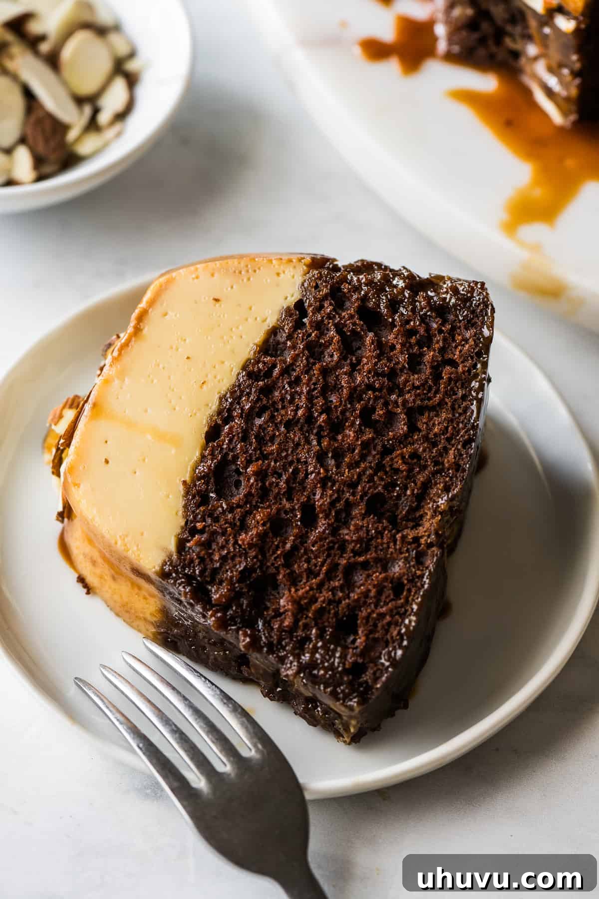 Chocolate Flan Fusion 13 A perfectly portioned slice of chocoflan on a white plate, revealing the distinct layers of chocolate cake and creamy flan, garnished with caramel.