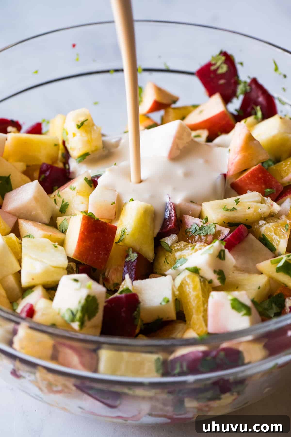 Yuletide Celebration Salad 5 Pouring the creamy sweet dressing over a bowl of mixed fruit and vegetable salad for Ensalada de Nochebuena, ensuring all ingredients are well coated.