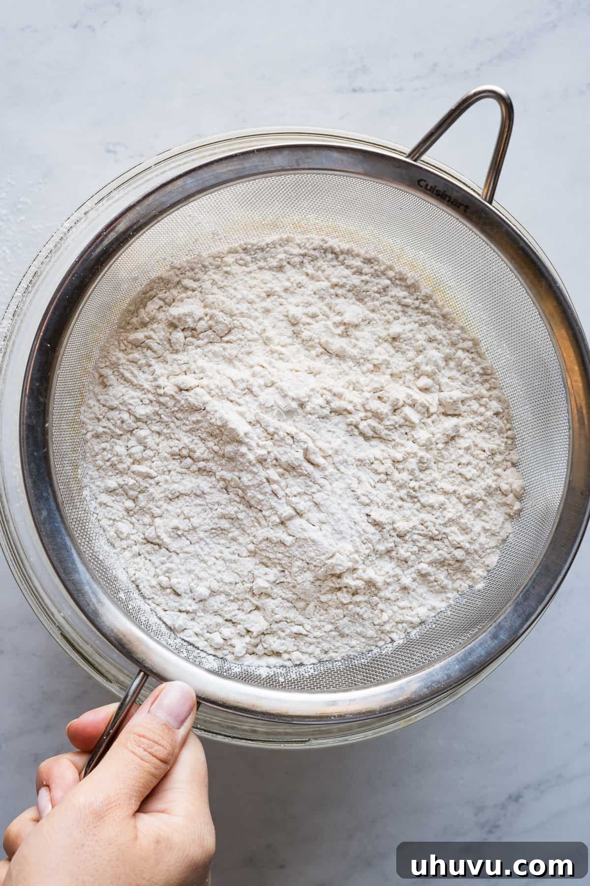 Spanish Muffins 6 All-purpose flour being sifted through a fine mesh strainer into a bowl of wet ingredients.