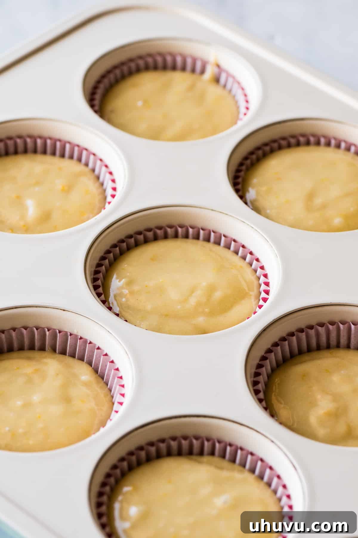 Spanish Muffins 8 Mantecada batter evenly filled into a muffin tin lined with red cupcake liners.