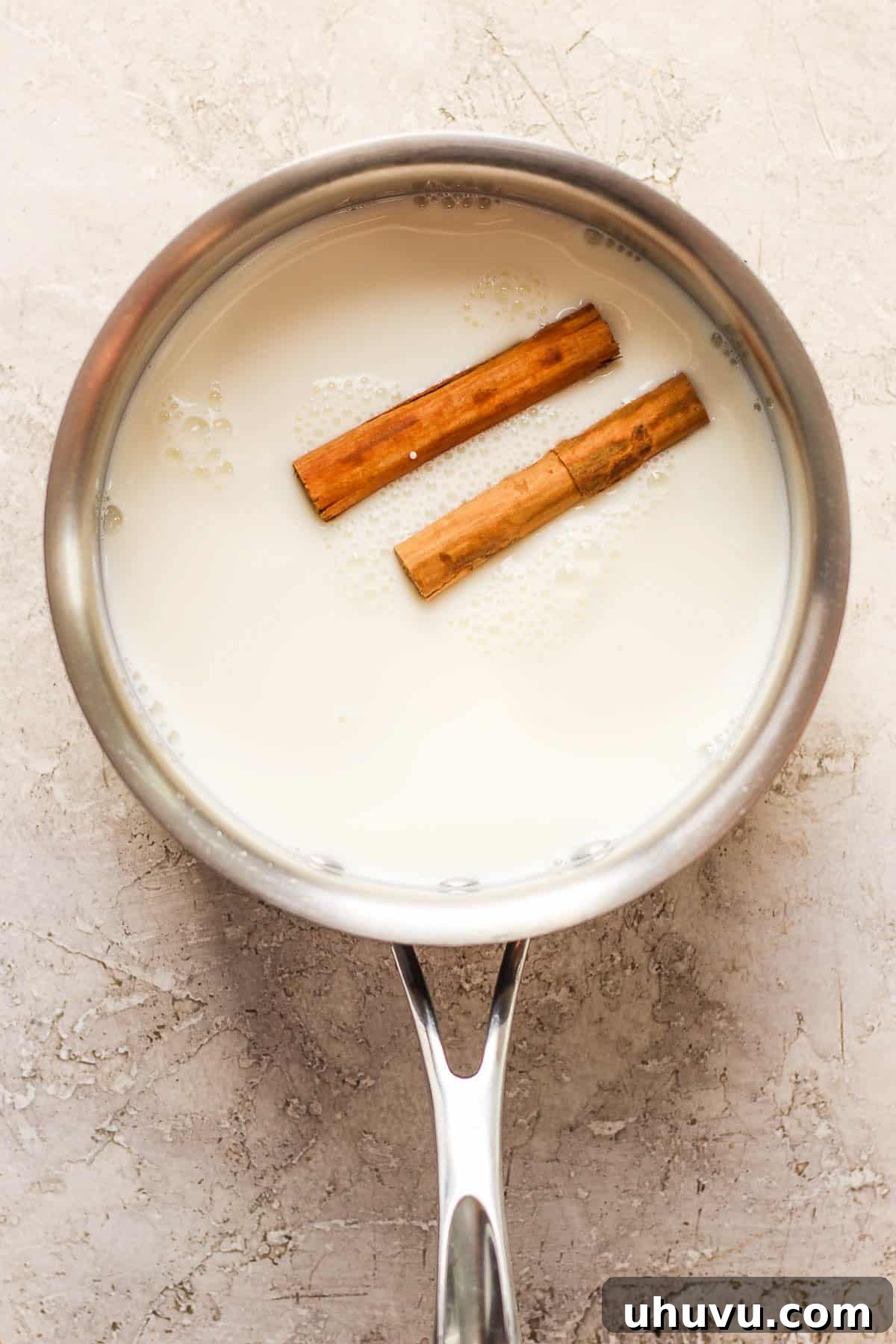 Homestyle María Biscuit Atole 4 Milk and cinnamon sticks in a small pot.