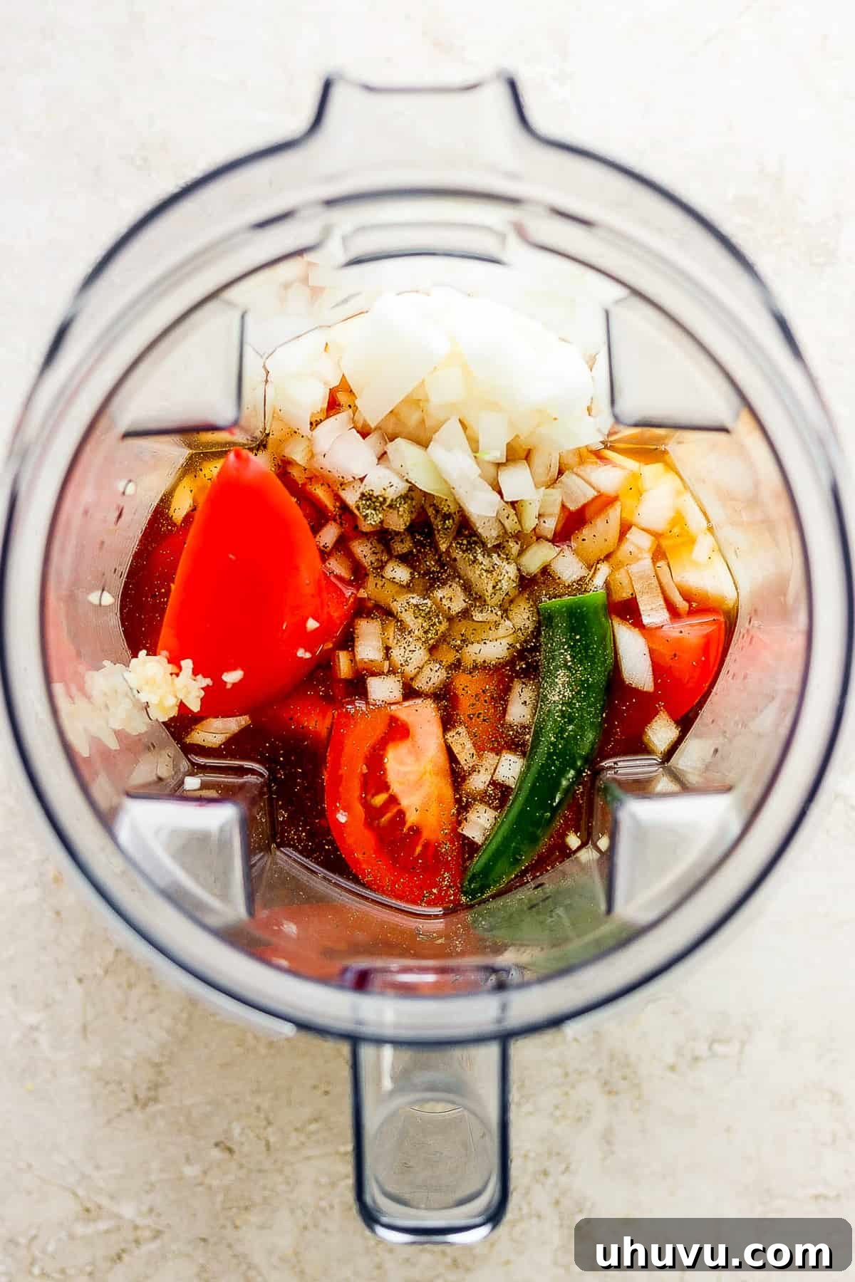 Homestyle Beef and Potatoes 5 Fresh ingredients including tomatoes, onion, serrano pepper, and garlic, along with beef broth, arranged inside a large blender, ready to be pureed into the stew's sauce.