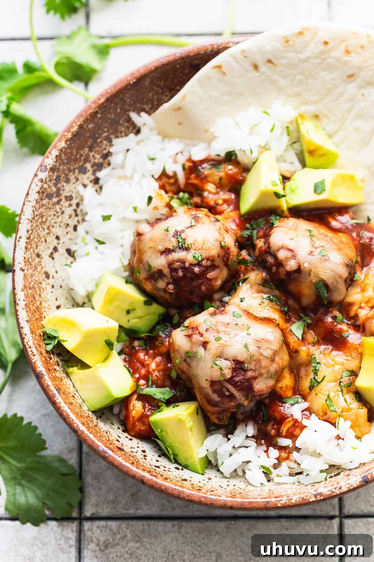 Smothered Enchilada Meatballs 8 Enchilada meatballs in a bowl with white rice and garnished with diced avocado.