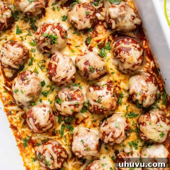 Enchilada meatballs baked in dish topped with cheese, cilantro, and enchilada sauce.