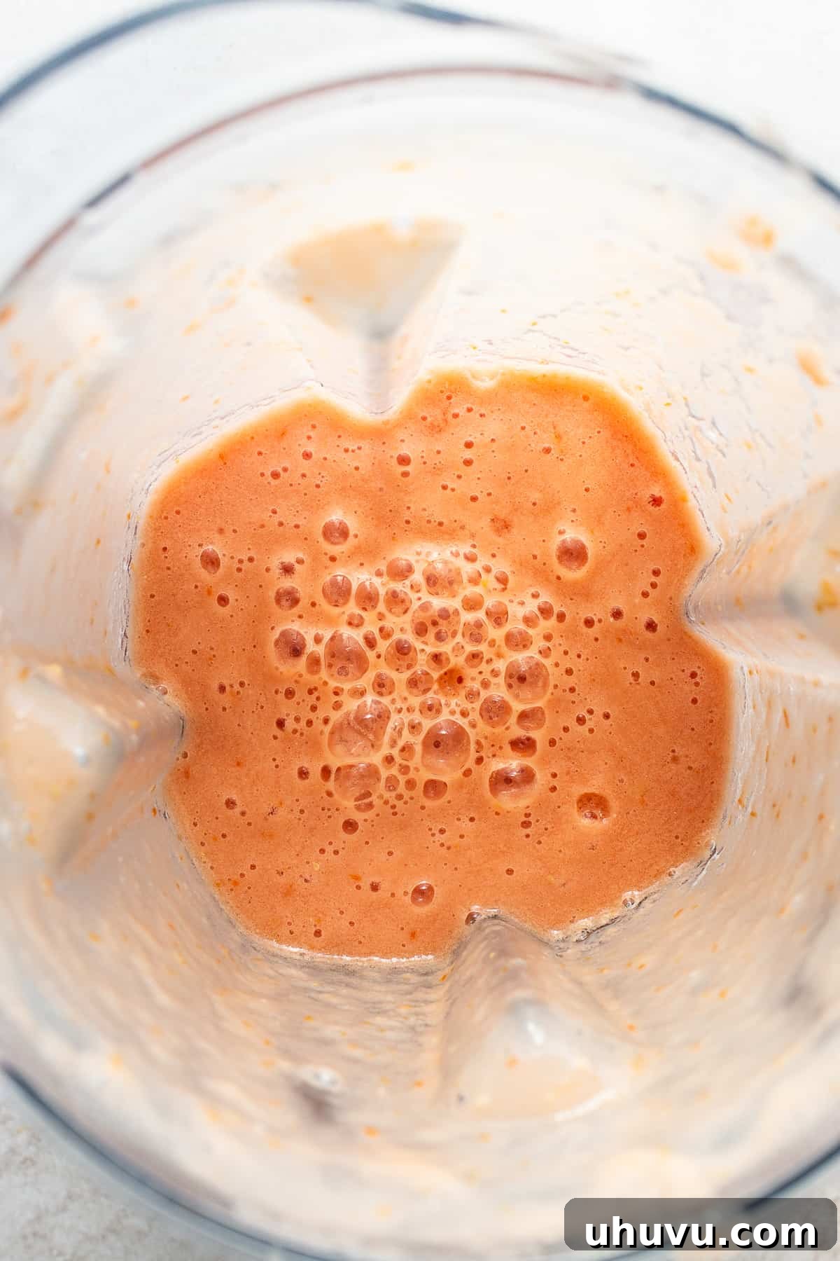 A close-up shot of a smooth, reddish-orange blended tomato and onion mixture inside a blender, ready to be added to the soup.