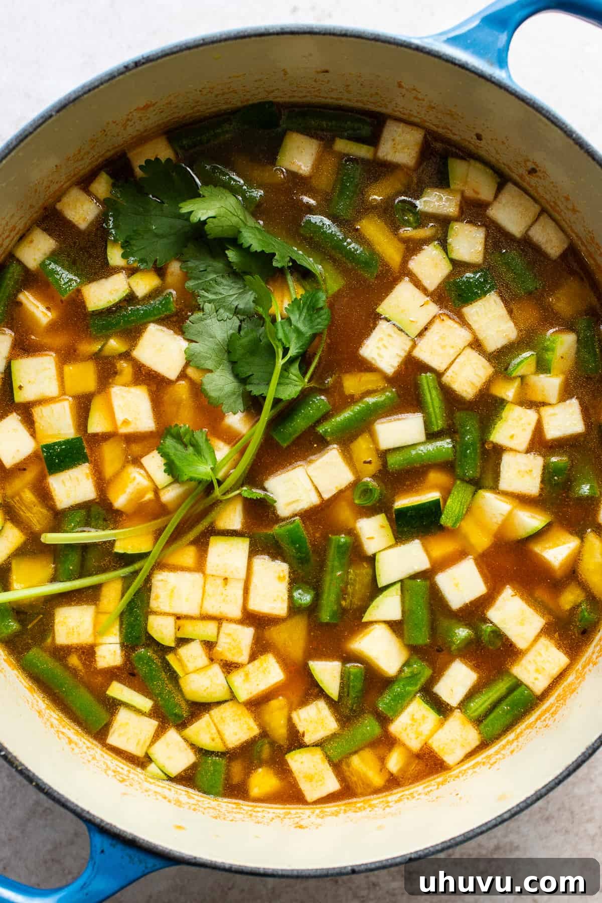 A Dutch oven filled with a colorful medley of diced vegetables and a vibrant red broth, simmering gently on the stovetop.