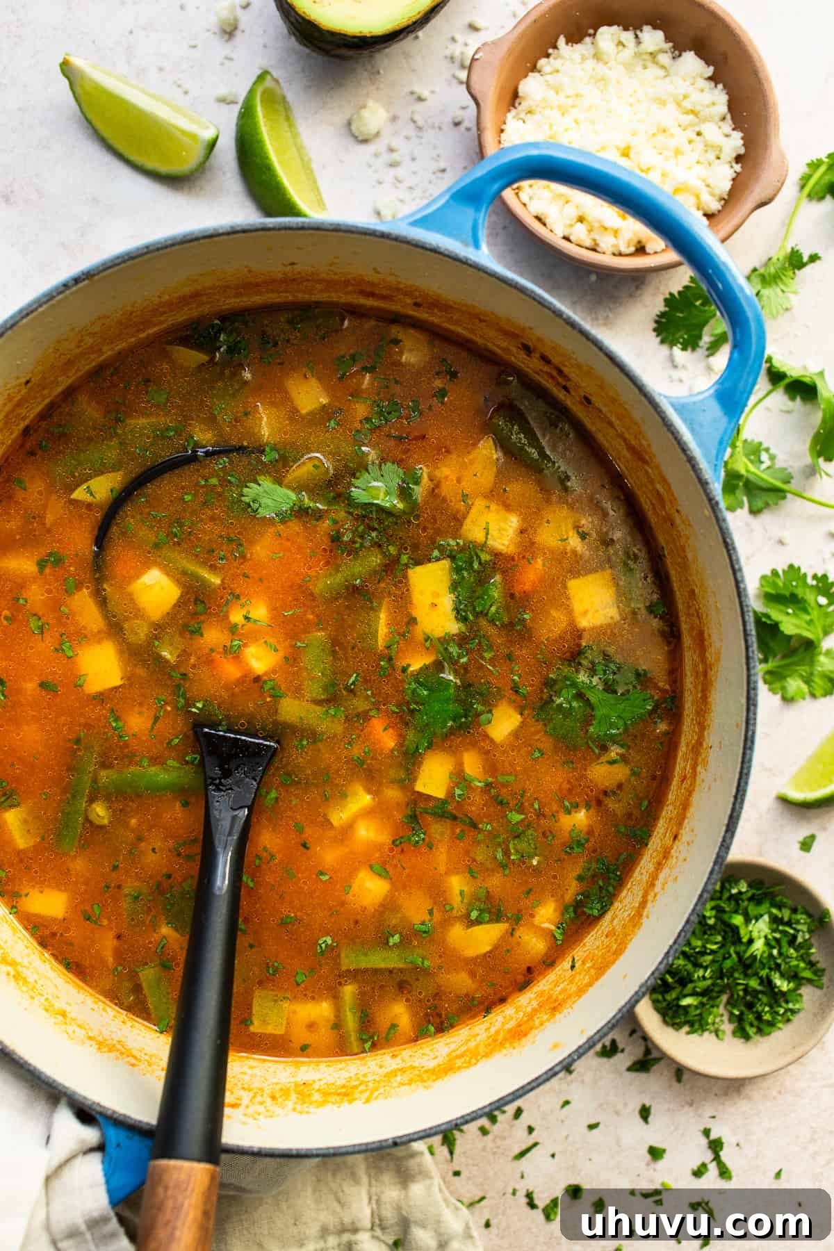 A large, rustic Dutch oven filled with Mexican Vegetable Soup, a ladle poised to serve, showcasing the rich broth and colorful vegetables.
