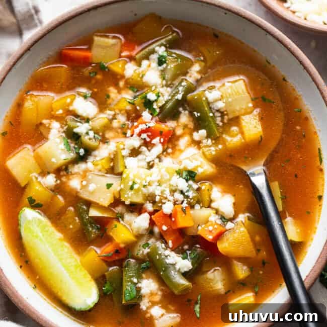 Mexican Vegetable Soup in a bowl garnished with lime juice and cotija cheese.