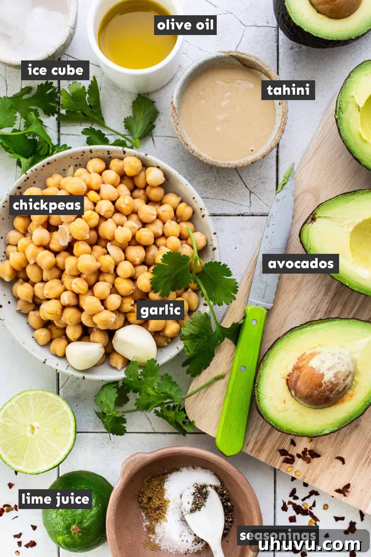 Green Goddess Hummus 3 Various ingredients for avocado hummus, including ripe avocados, chickpeas, tahini, lime, and spices, arranged on a rustic wooden table.