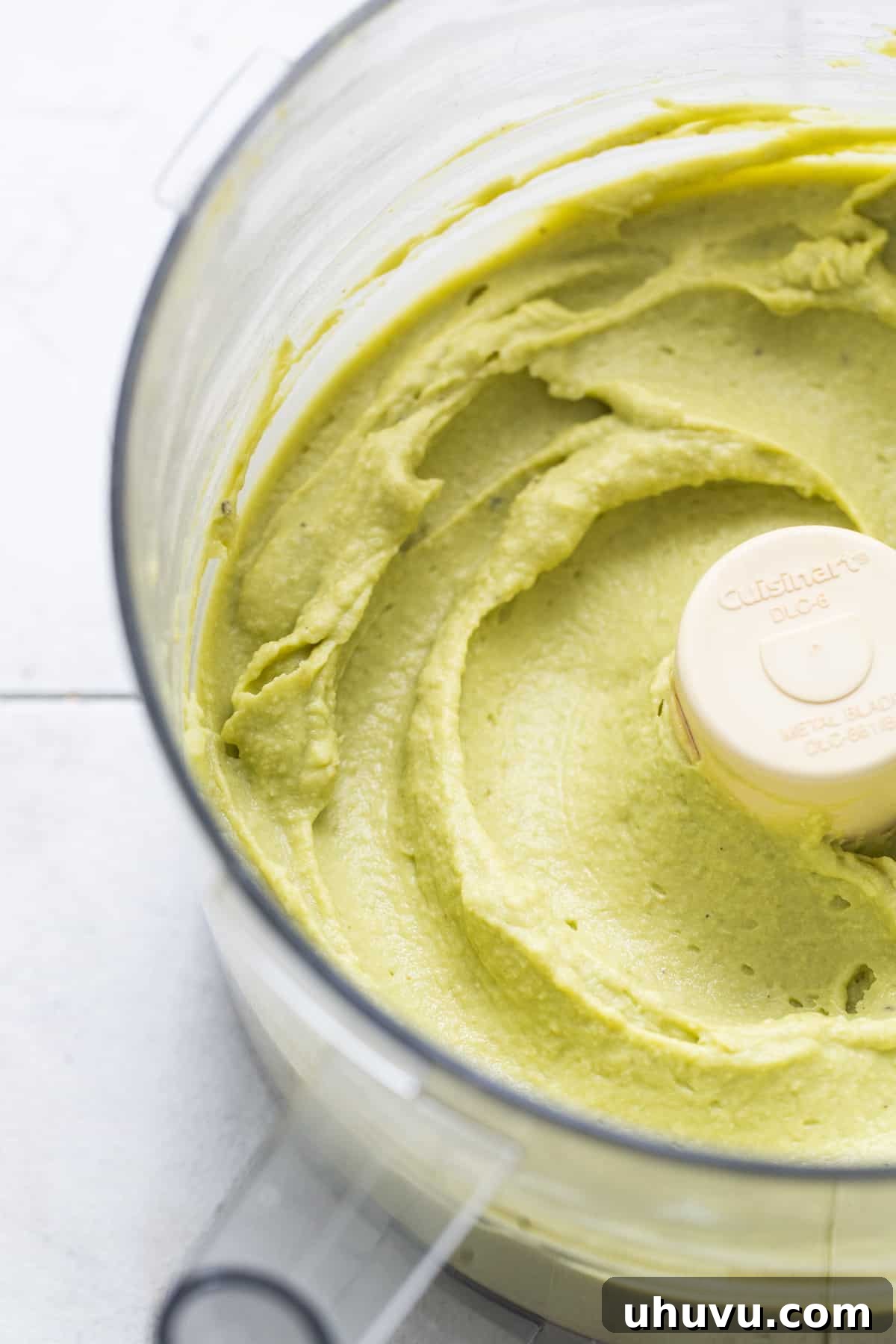 Green Goddess Hummus 6 A close-up shot of perfectly smooth and creamy avocado hummus filling the bowl of a food processor.