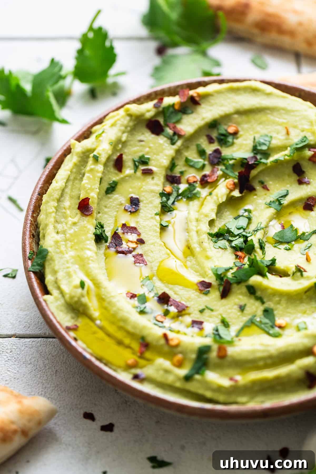 Green Goddess Hummus 7 A bowl of creamy avocado hummus, beautifully garnished with a drizzle of olive oil, vibrant chopped cilantro, and a sprinkle of crushed red pepper flakes.
