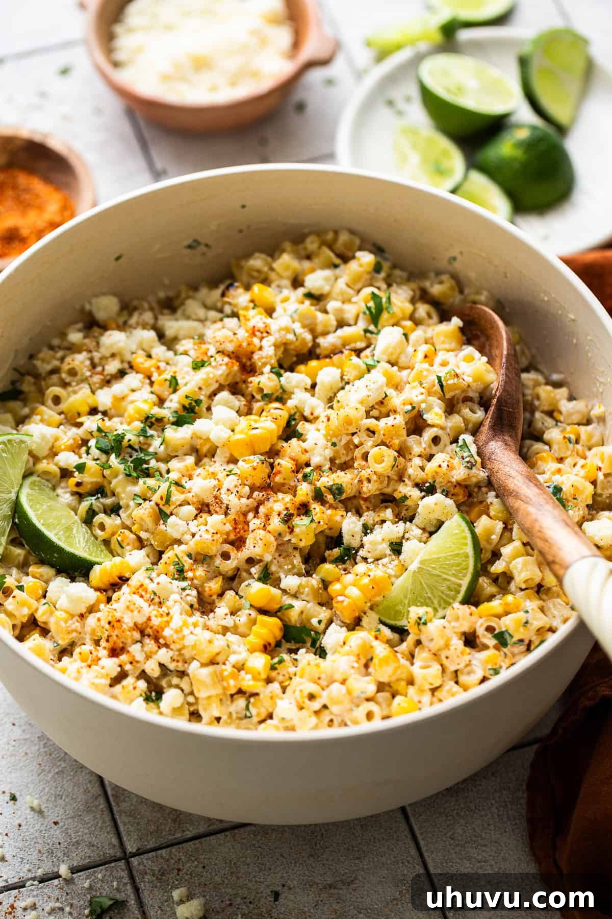 A close-up of the finished Mexican Street Corn Pasta Salad in a serving bowl, garnished with extra cilantro, cotija cheese, and a vibrant sprinkle of Tajín seasoning.