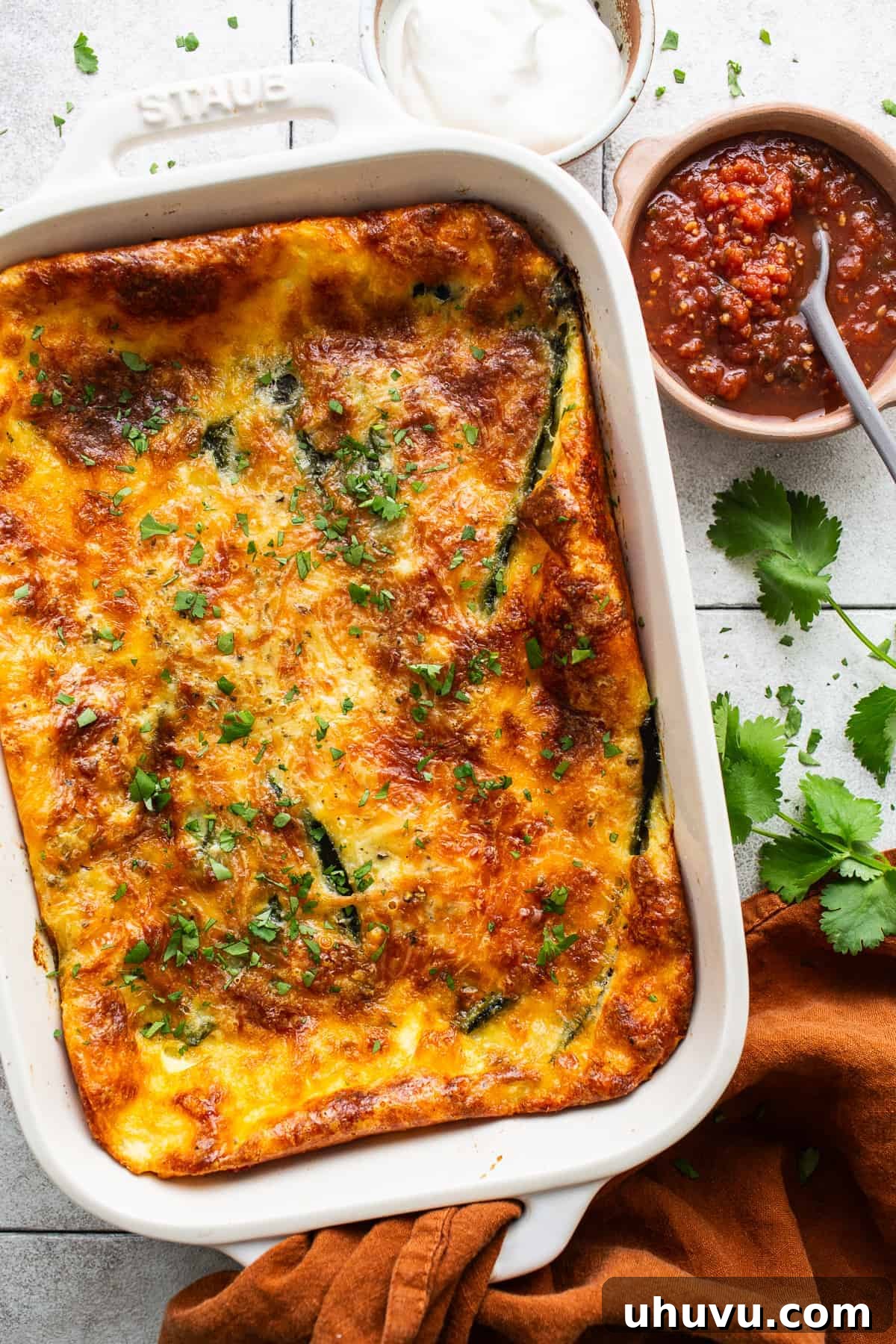 A close-up shot of a steaming, golden-brown casserole, likely a chile relleno casserole, topped with melted cheese and ready to be served, making mouths water.
