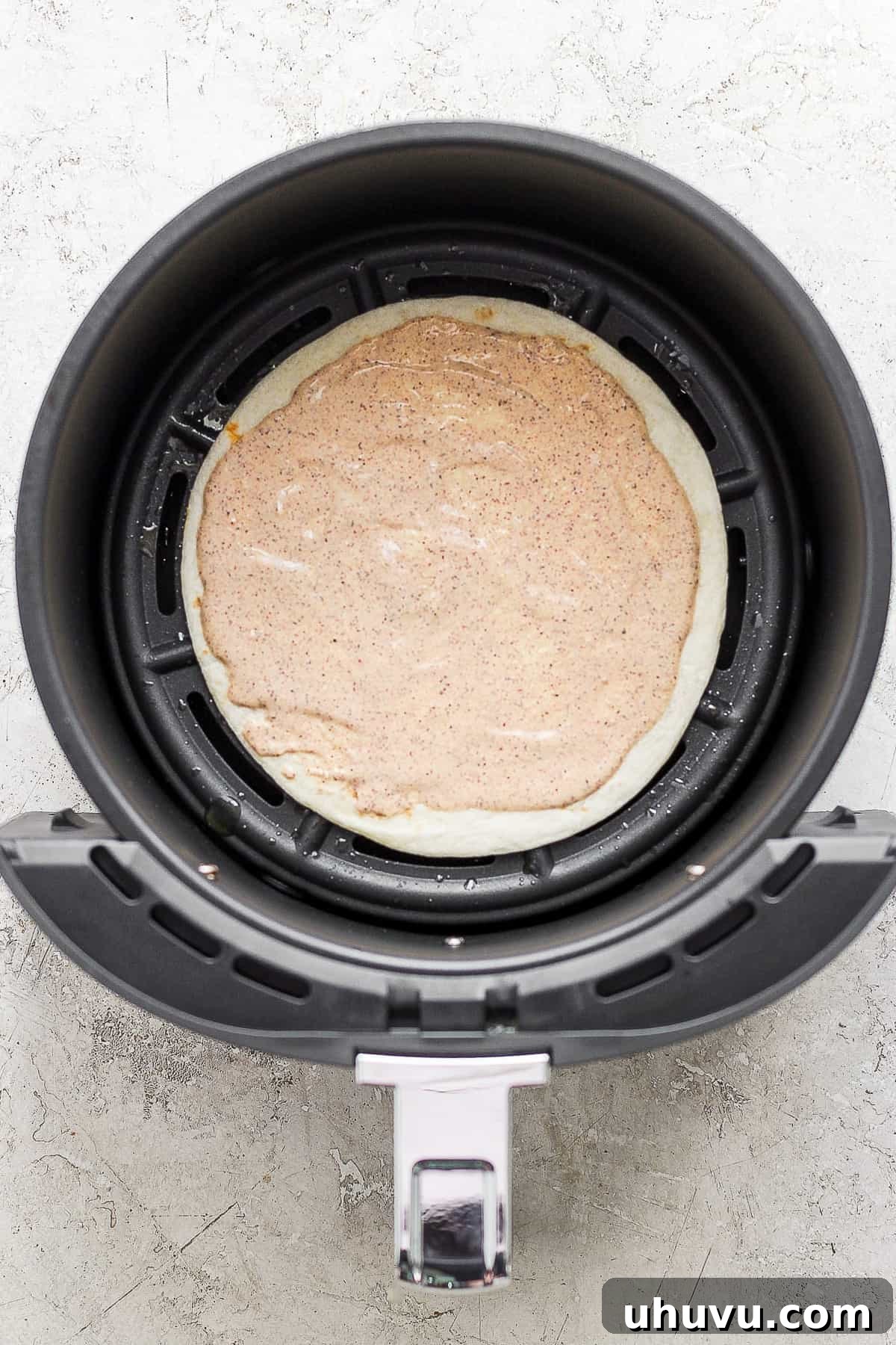 Crispy Air Fryer Chicken Quesadillas 5 A single flour tortilla, partially covered with a creamy chili-lime sauce, resting inside an air fryer basket.