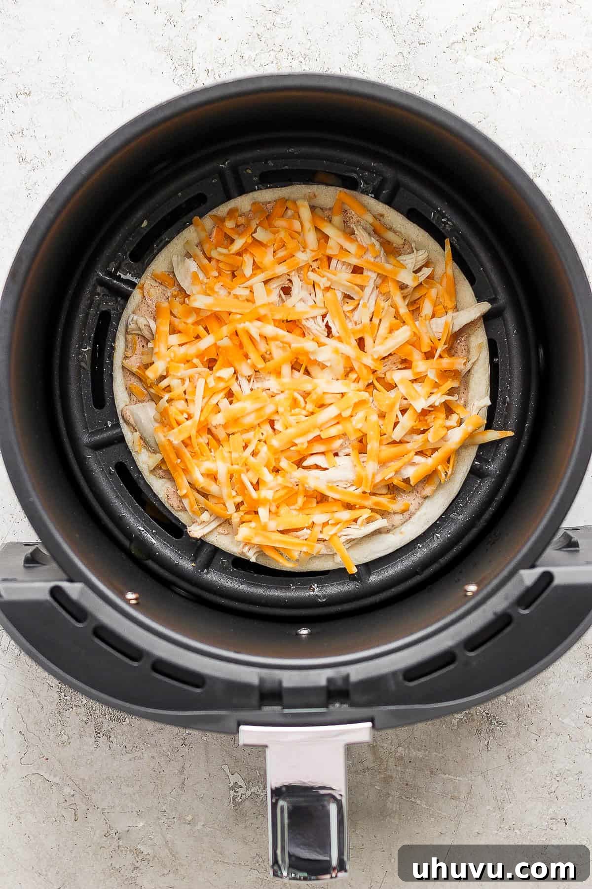 Crispy Air Fryer Chicken Quesadillas 6 Shredded chicken and a generous layer of shredded cheese are spread over a sauce-covered flour tortilla within an air fryer, ready for the top tortilla.