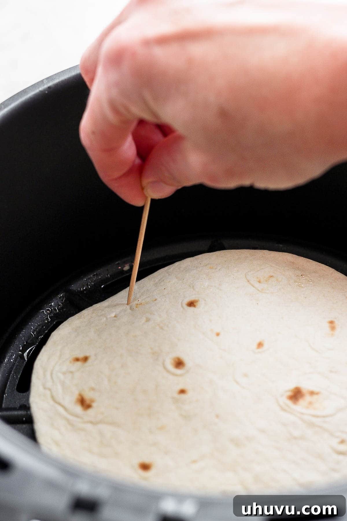 Crispy Air Fryer Chicken Quesadillas 7 A chicken quesadilla secured with toothpicks along its edges, placed in an air fryer basket, ready for cooking.
