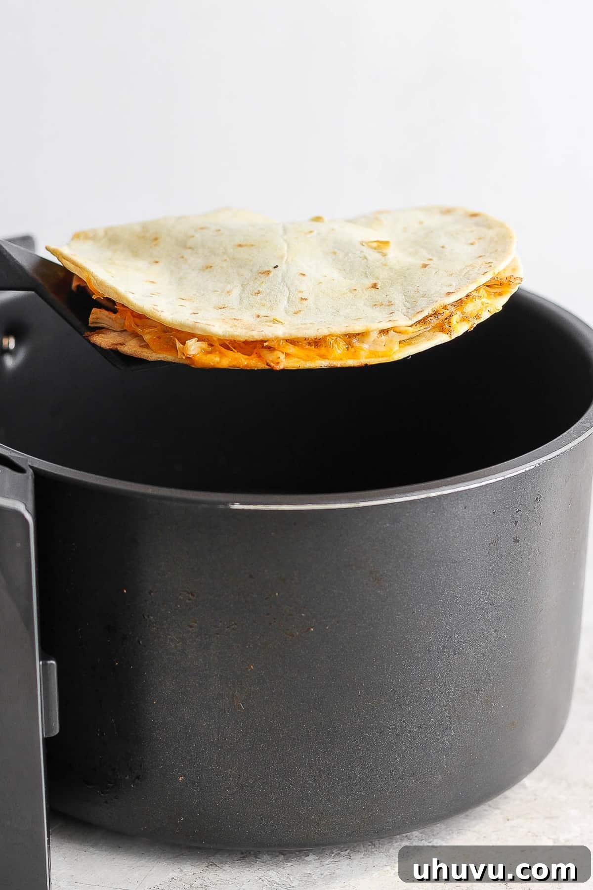 Crispy Air Fryer Chicken Quesadillas 8 A perfectly cooked, golden-brown quesadilla being carefully removed from an air fryer basket with tongs.