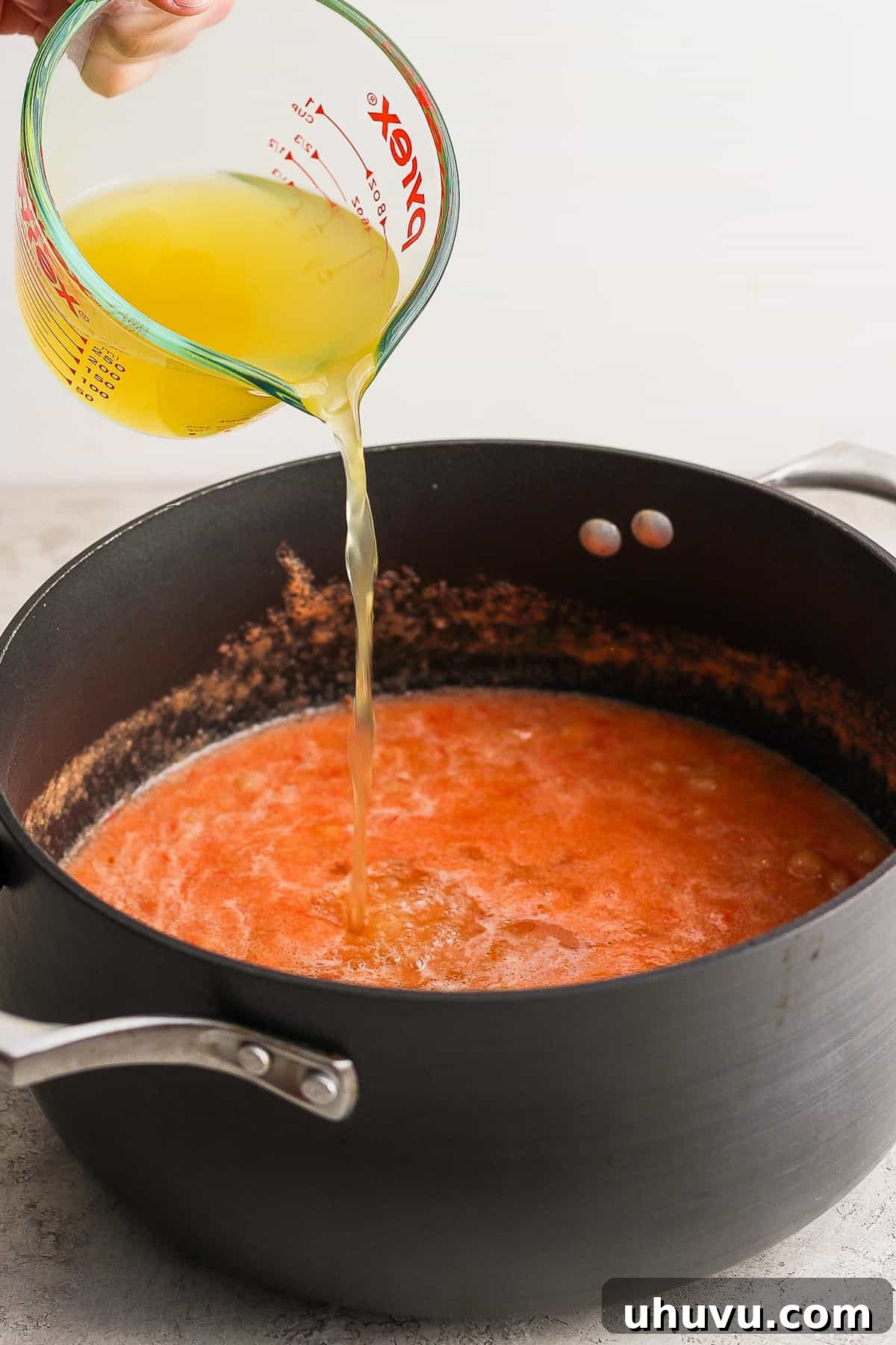Little Shell Pasta Soup 7 Clear vegetable broth being poured into a pot of simmering Sopa de Conchas, blending with the rich tomato-pasta mixture.