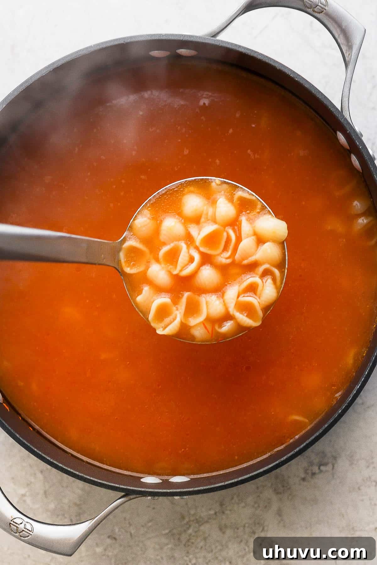 Little Shell Pasta Soup 8 A ladle gracefully scooping a portion of steaming, brothy Sopa de Conchas from a pot, highlighting the tender pasta.