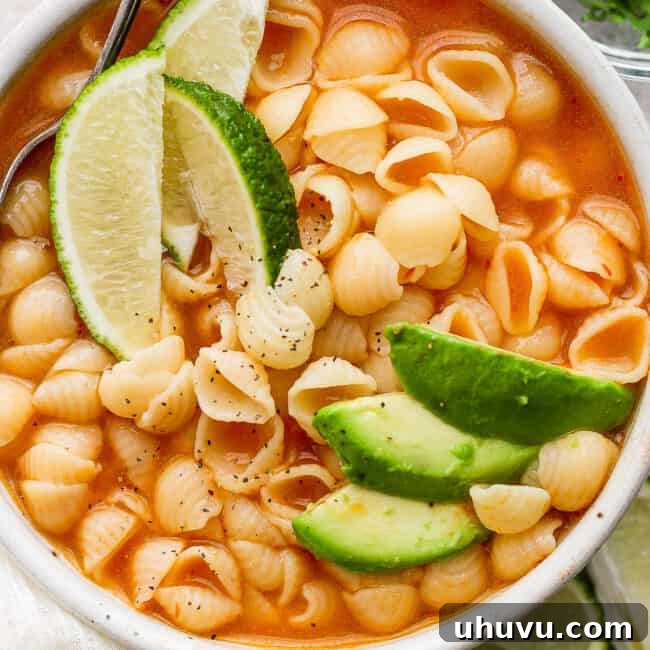 Sopa de conchas in a white bowl topped with sliced avocado.