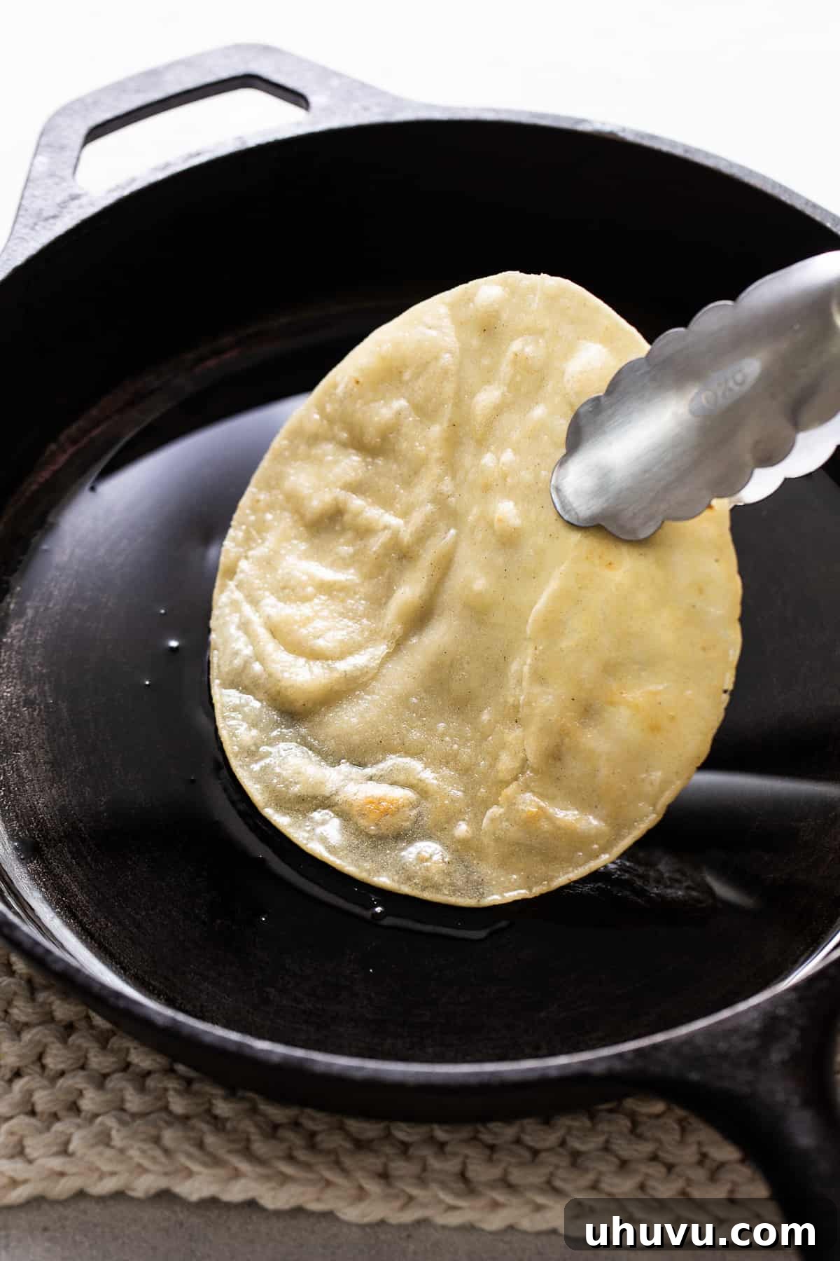 Mexican Mole Bliss 5 A single corn tortilla gently frying in a pan with hot oil, its edges just starting to crisp and soften, preparing it for the enmolada assembly.